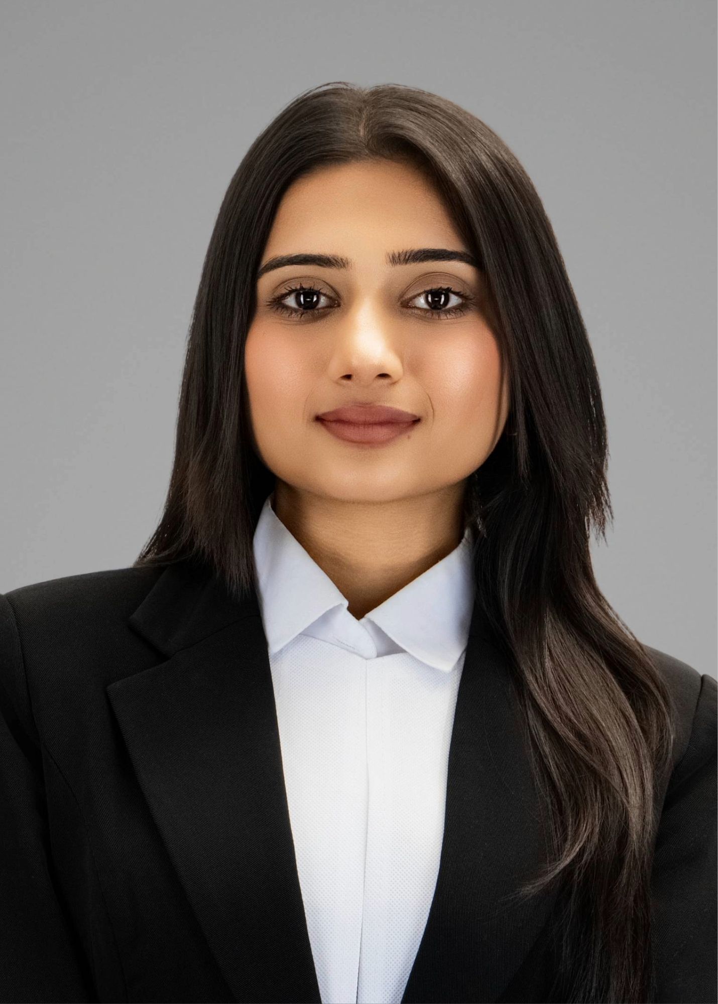 Professional headshot of a young woman in a black blazer and white shirt with long dark hair.