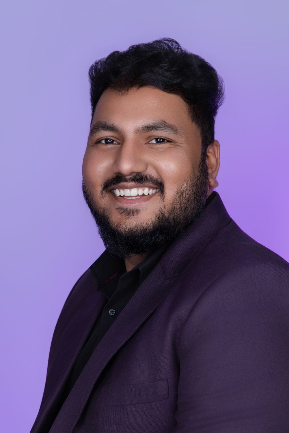 Professional studio portraits of someone in a dark suit jacket against a purple gradient background.