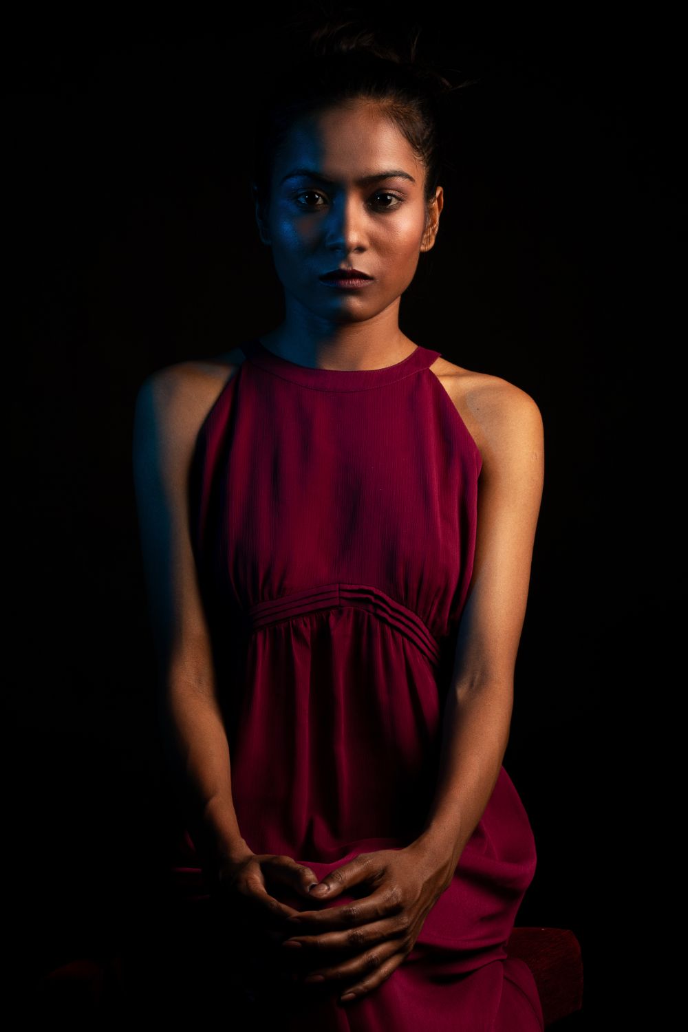 Dramatic portraits in burgundy sleeveless dress with moody lighting and shadows.