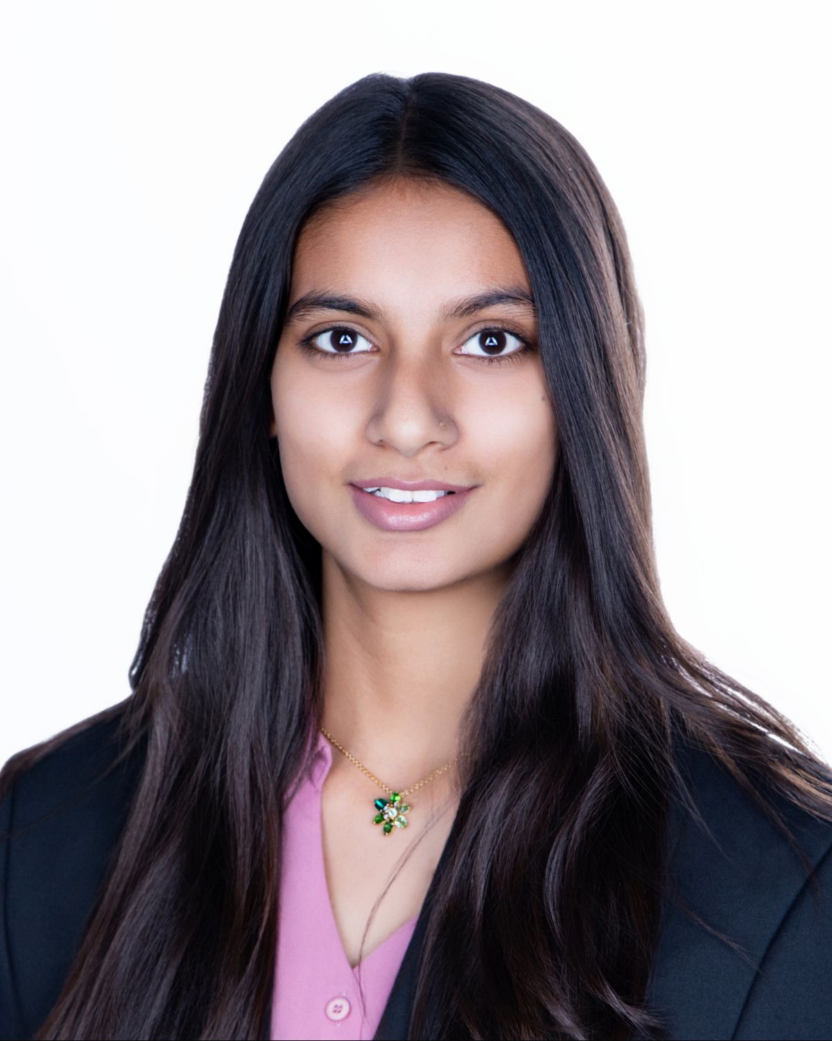 Young professional woman with long dark hair wearing a pink blouse and black blazer with a floral necklace.