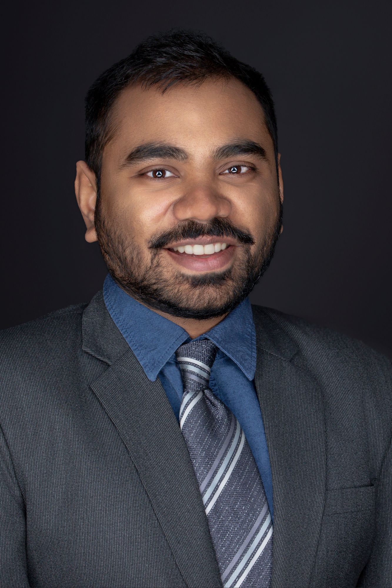 Professional headshots of person in gray suit and striped tie against dark background.