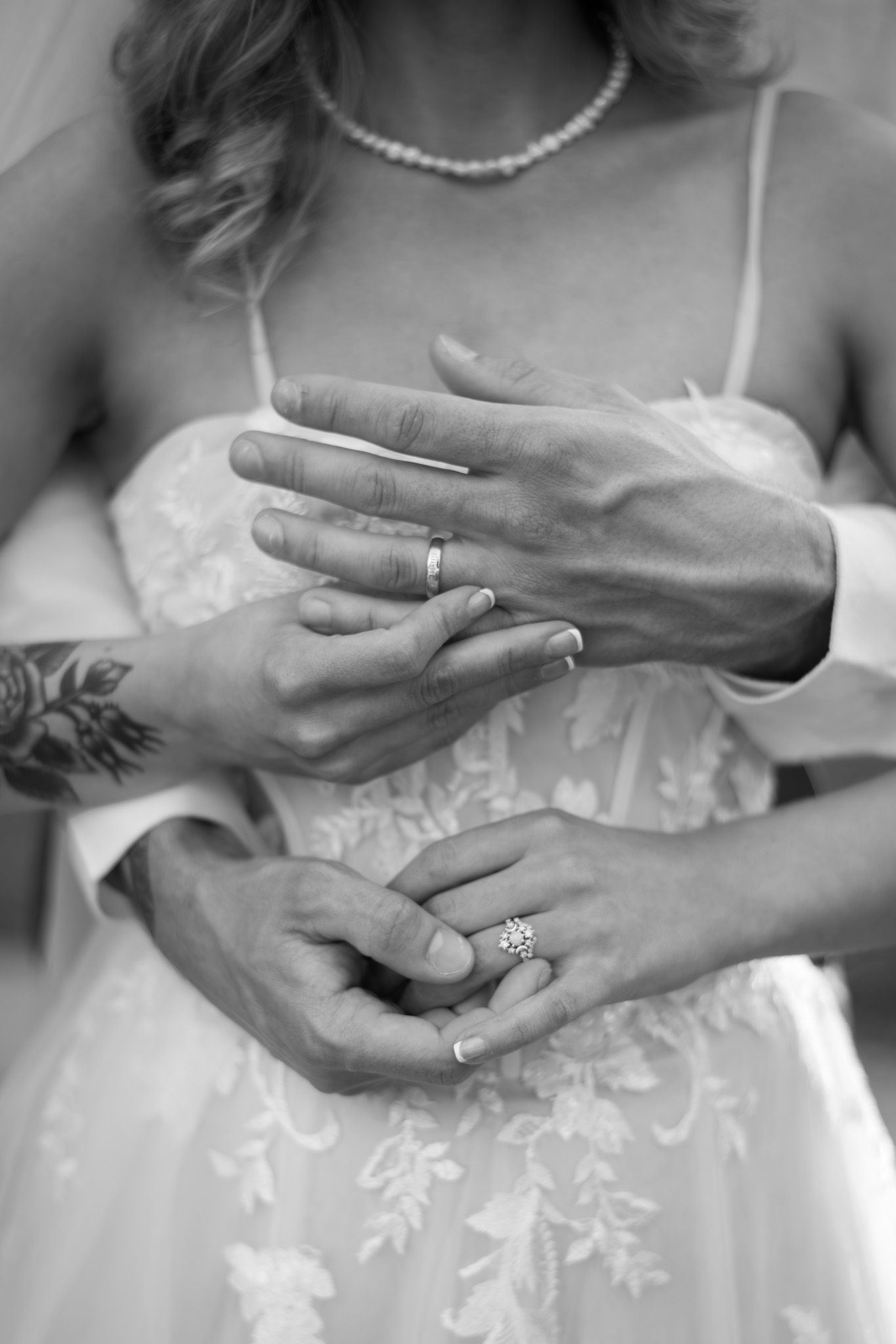 Close-up black and white photo of bride and groom displaying wedding rings together.