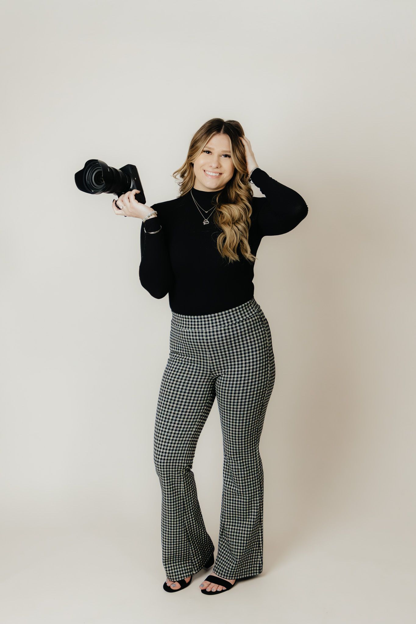 Female photographer in black top and houndstooth pants poses with professional camera.