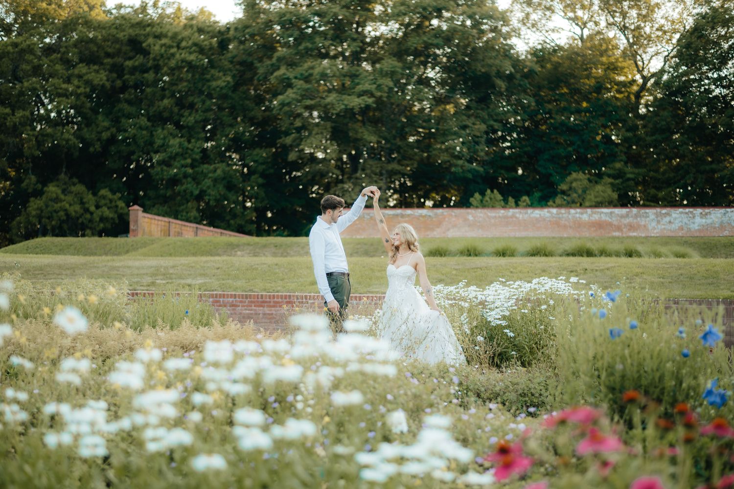 Bride and groom dancing in a wildflower meadow at golden hour with colorful blooms in the foreground.