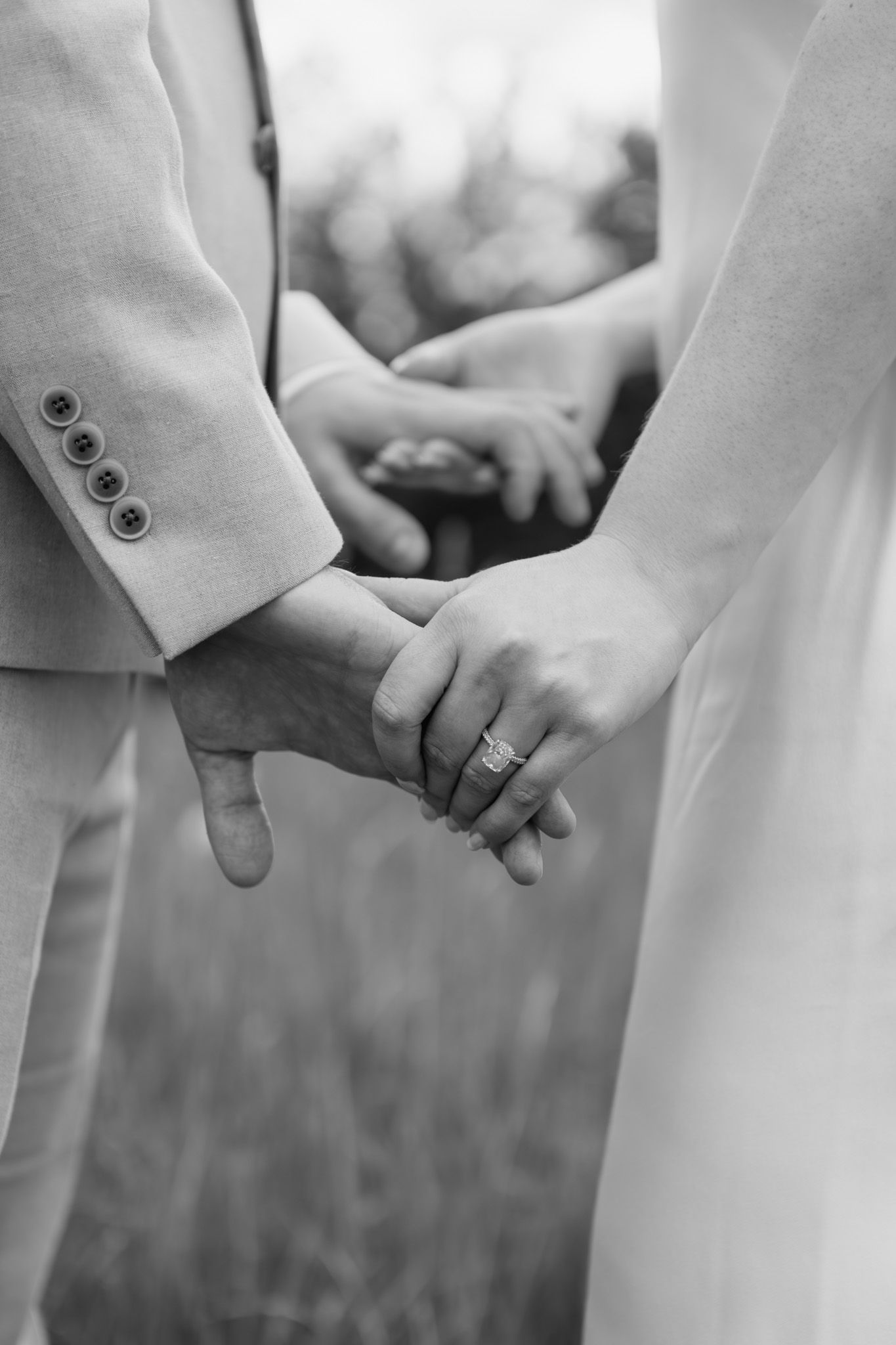 Black and white close-up of bride and groom holding hands showing wedding ring detail.