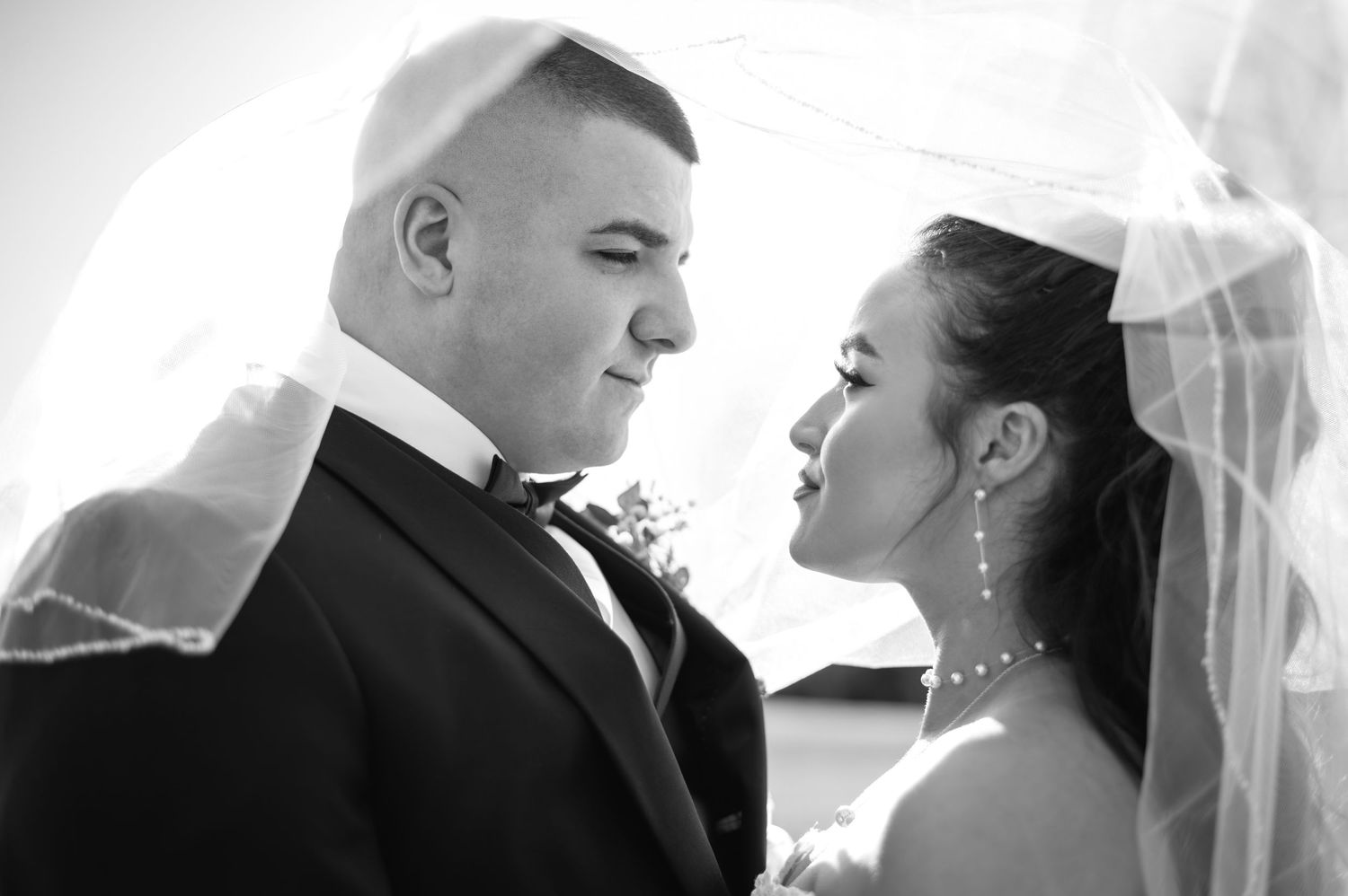 Black and white close-up of bride and groom gazing at each other beneath a flowing wedding veil.