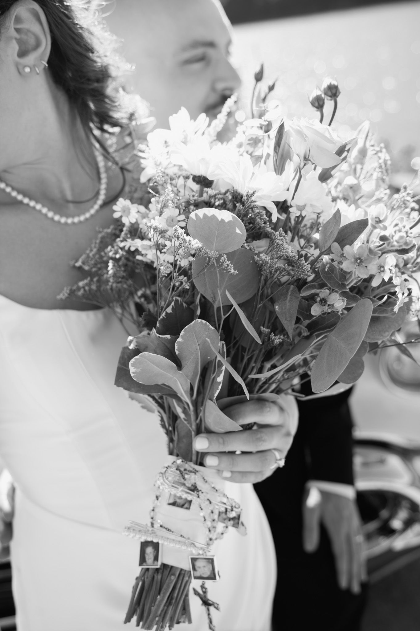 Black and white image of bride holding floral bouquet with sentimental photo charms attached to stems.