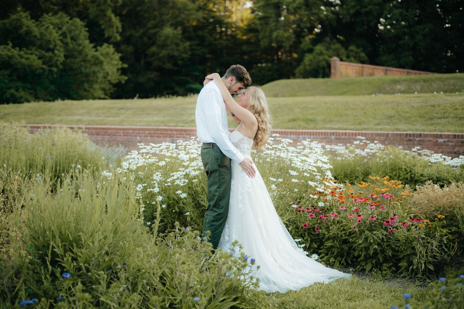 Bride and groom embrace romantically in a lush garden filled with wildflowers.