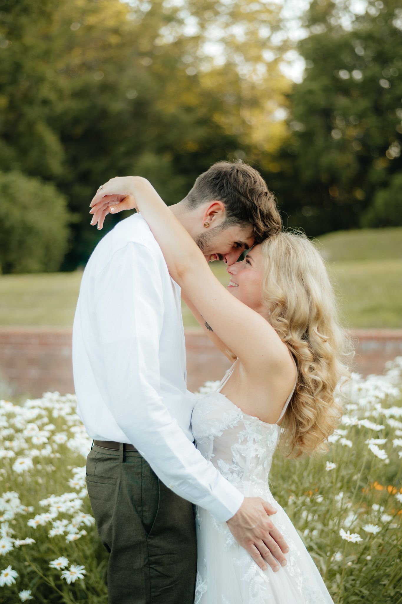 Bride and groom share a tender embrace in a blooming daisy field at sunset.