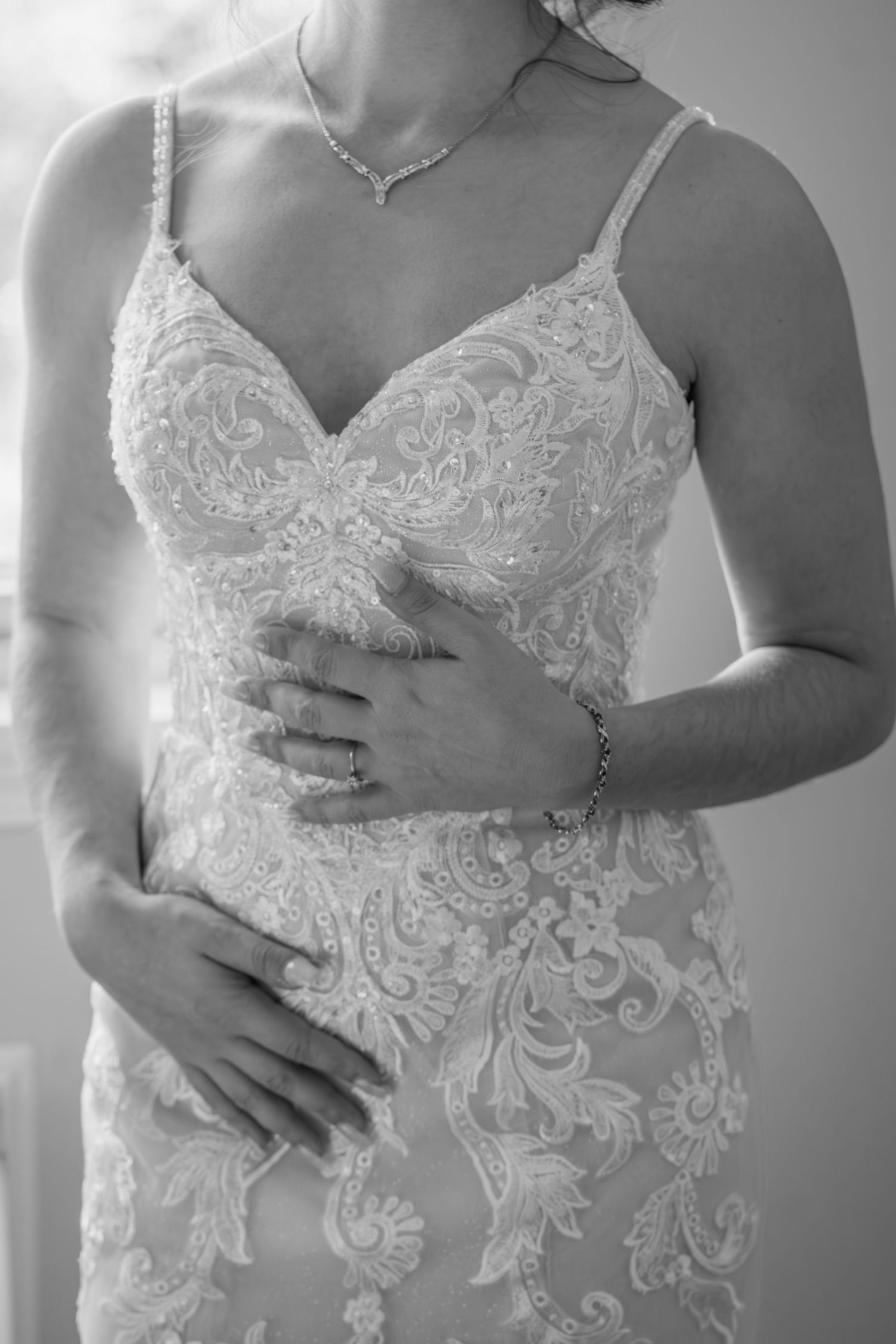Black and white close-up of a bride in a lace wedding gown with delicate spaghetti straps and jewelry.