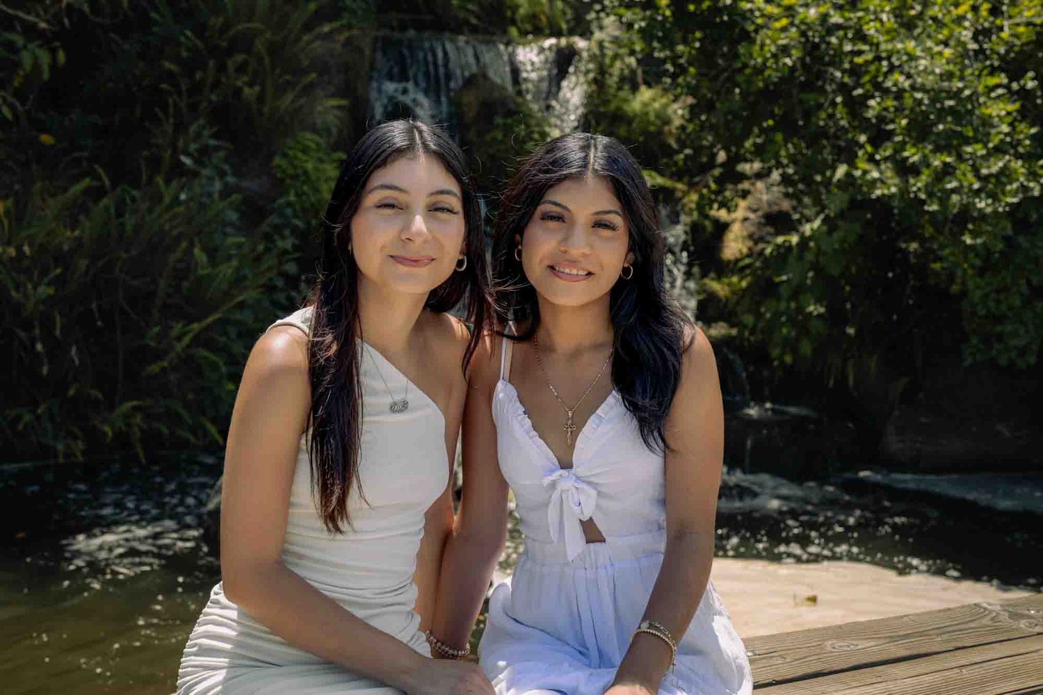 Two people in white tops pose together outdoors in a sunny garden setting.