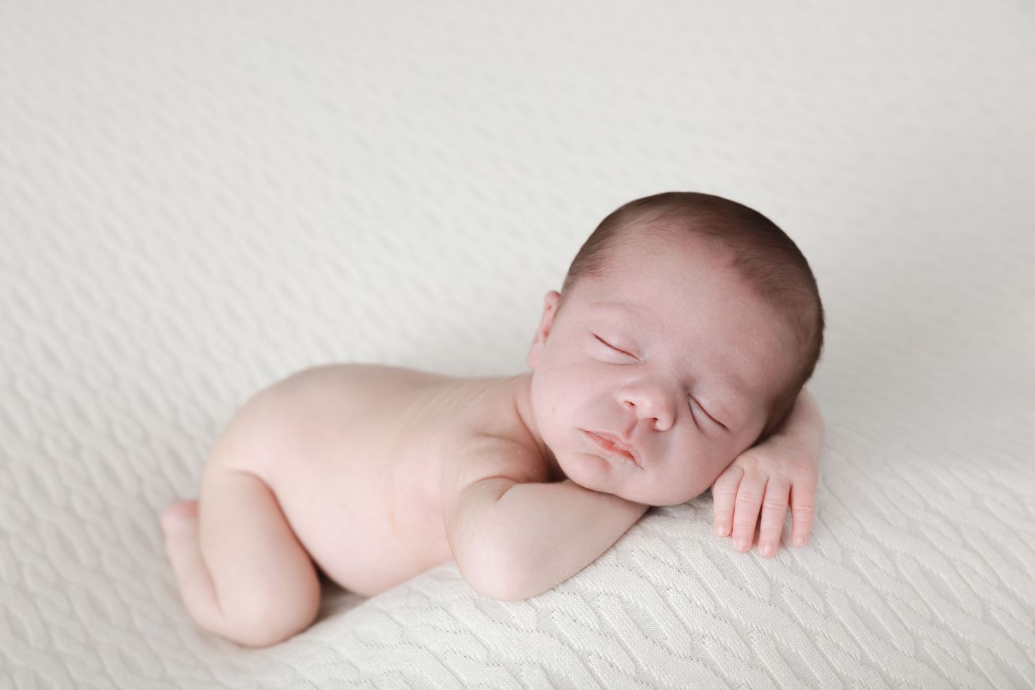 A sleeping newborn baby lies peacefully in a soft white blanket during a professional photography session.