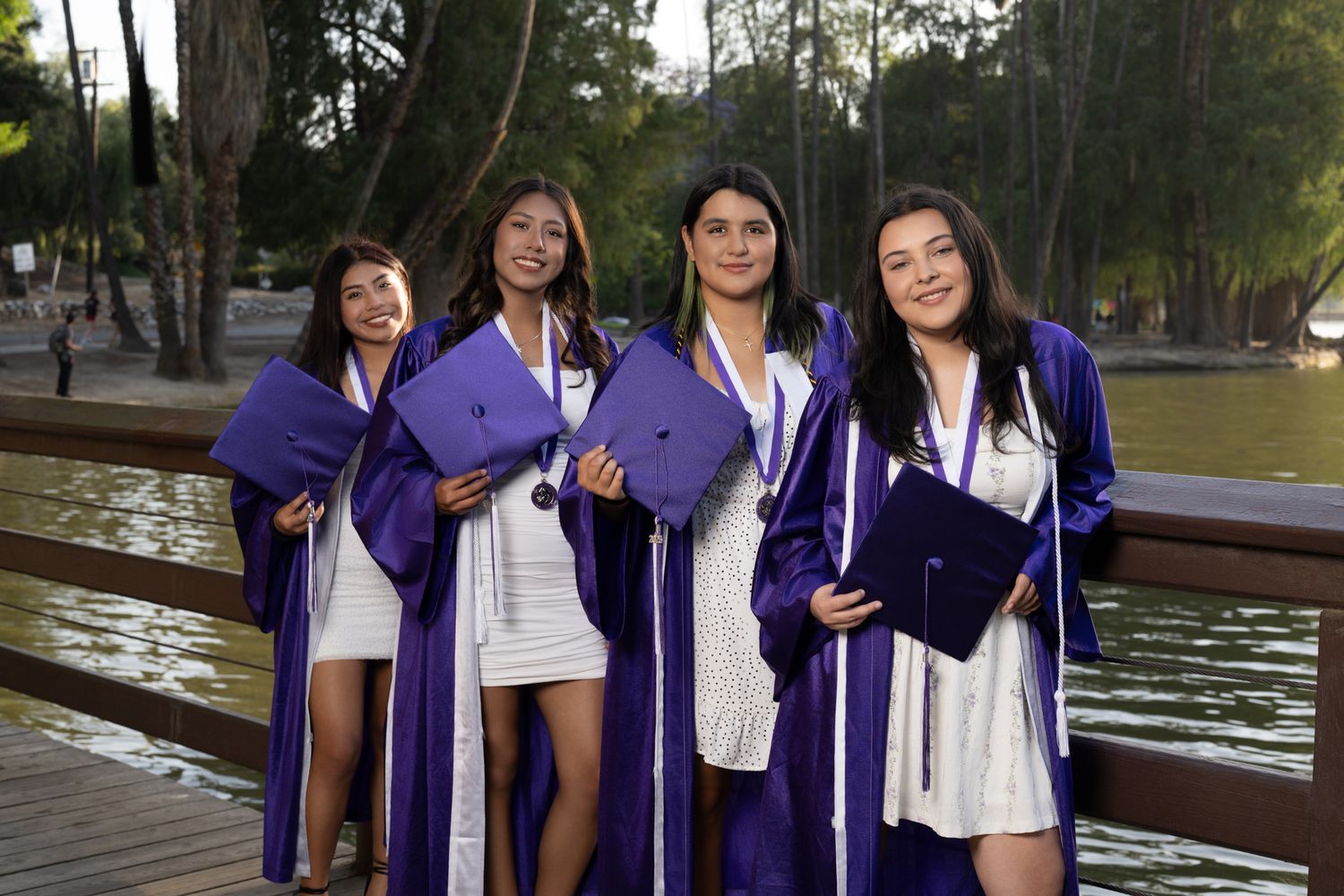 Group wearing matching purple graduation gowns pose together near a waterfront setting.