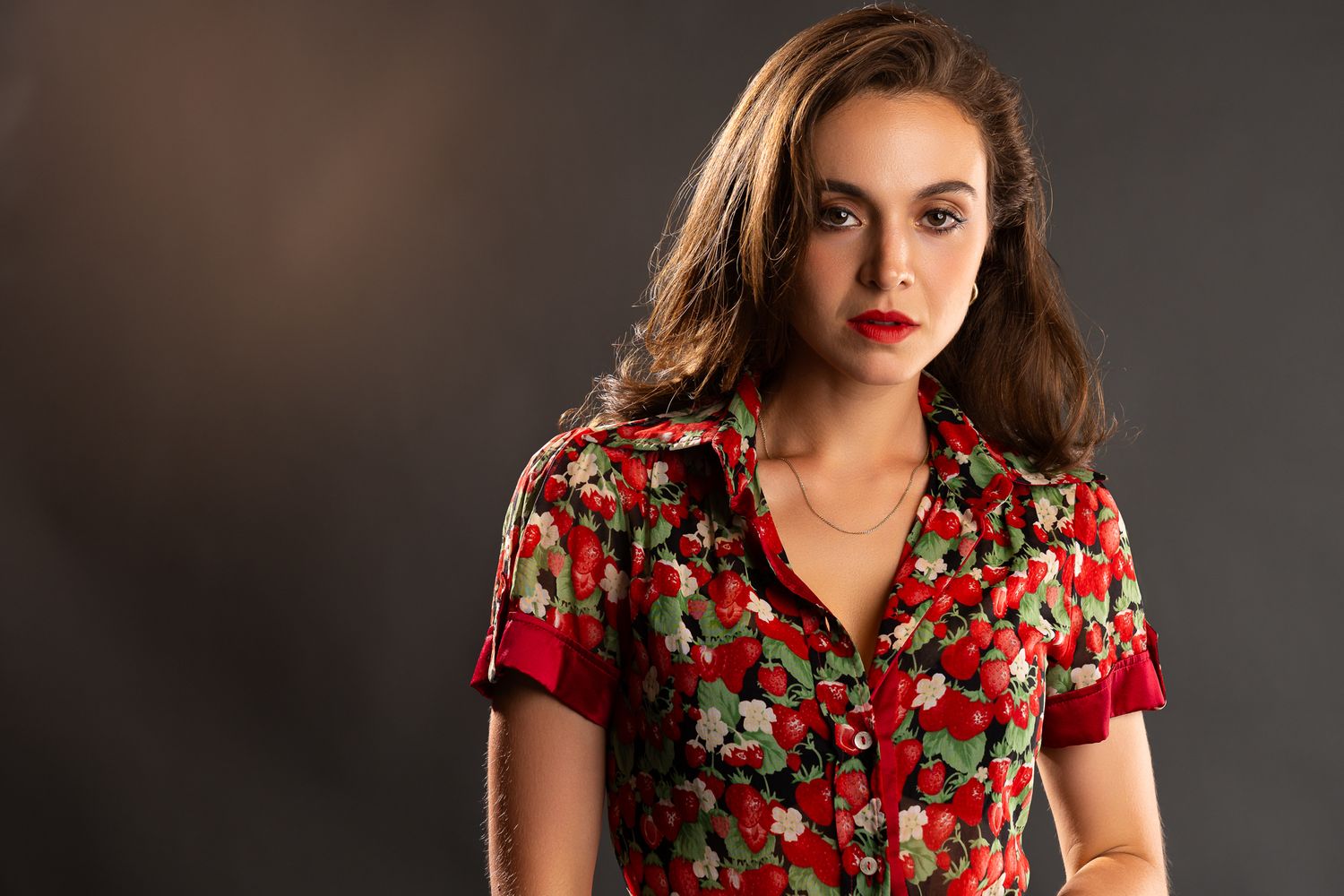 Woman in red floral dress poses confidently against dark background in professional studio photoshoot.