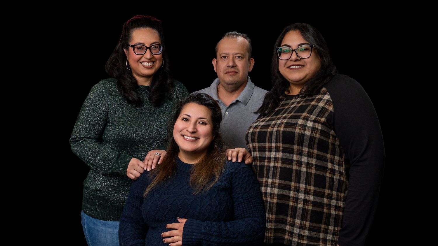 A group of four people pose together for a professional studio portrait against a black background.