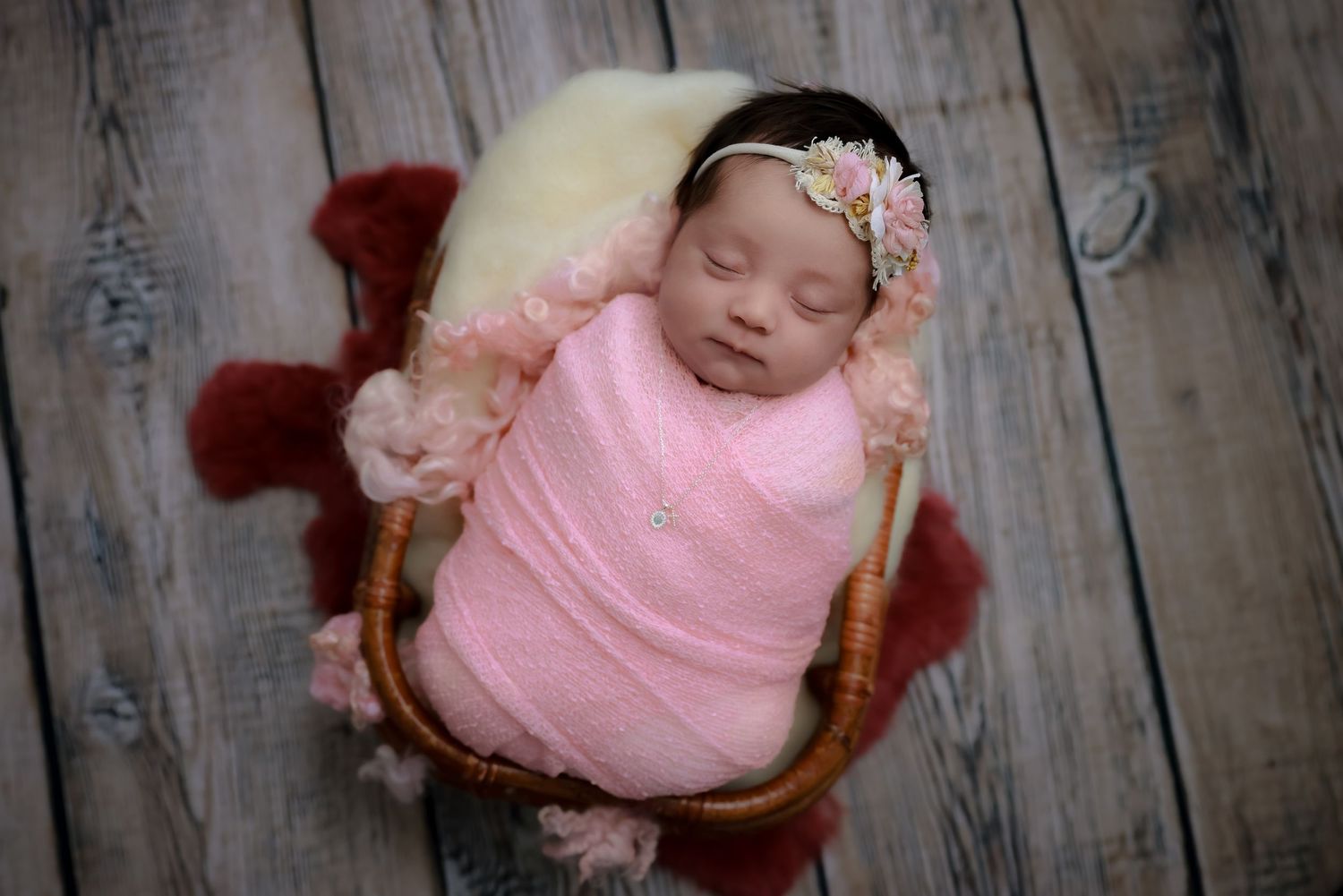 A sleeping baby wearing pink clothing rests peacefully on a rustic wooden background. luxury-family-photography-Claremont