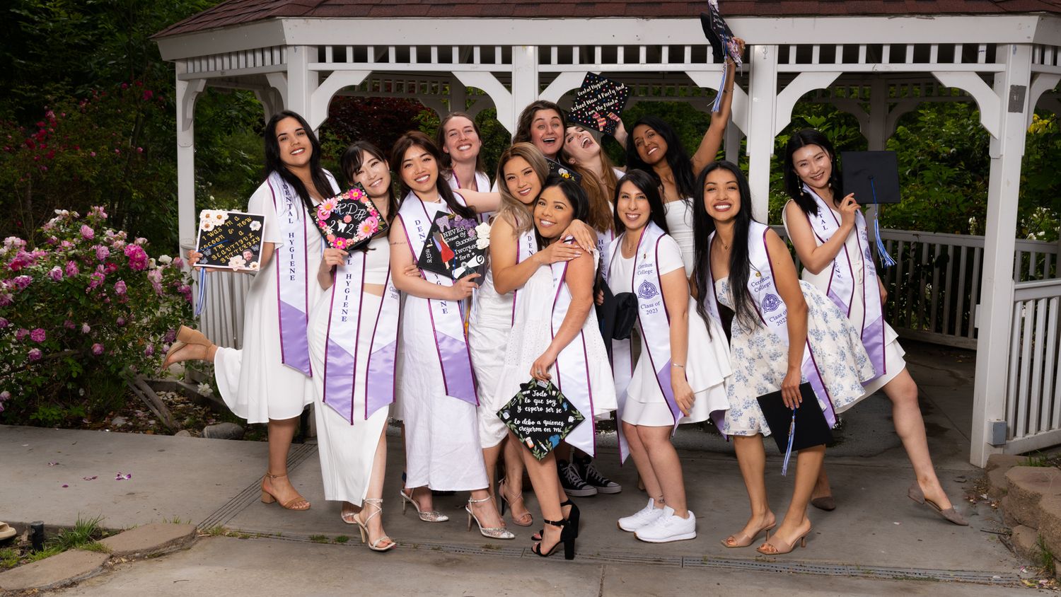A group in white outfits poses together on outdoor steps for a celebratory graduation photo.