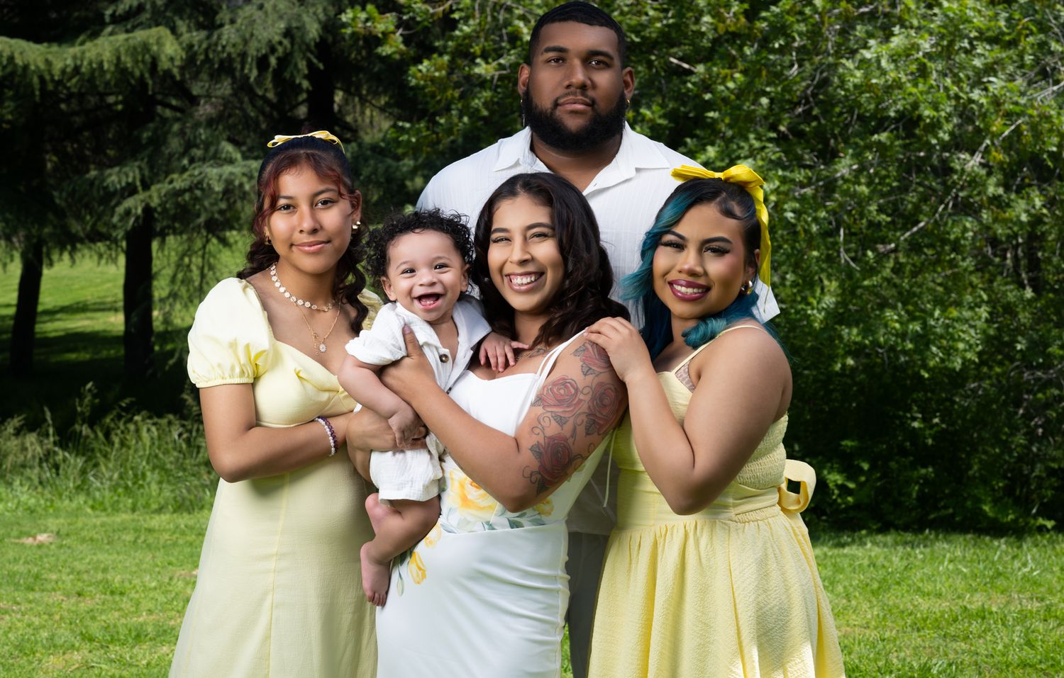 Family group photo in a lush green park setting wearing coordinated pastel outfits.