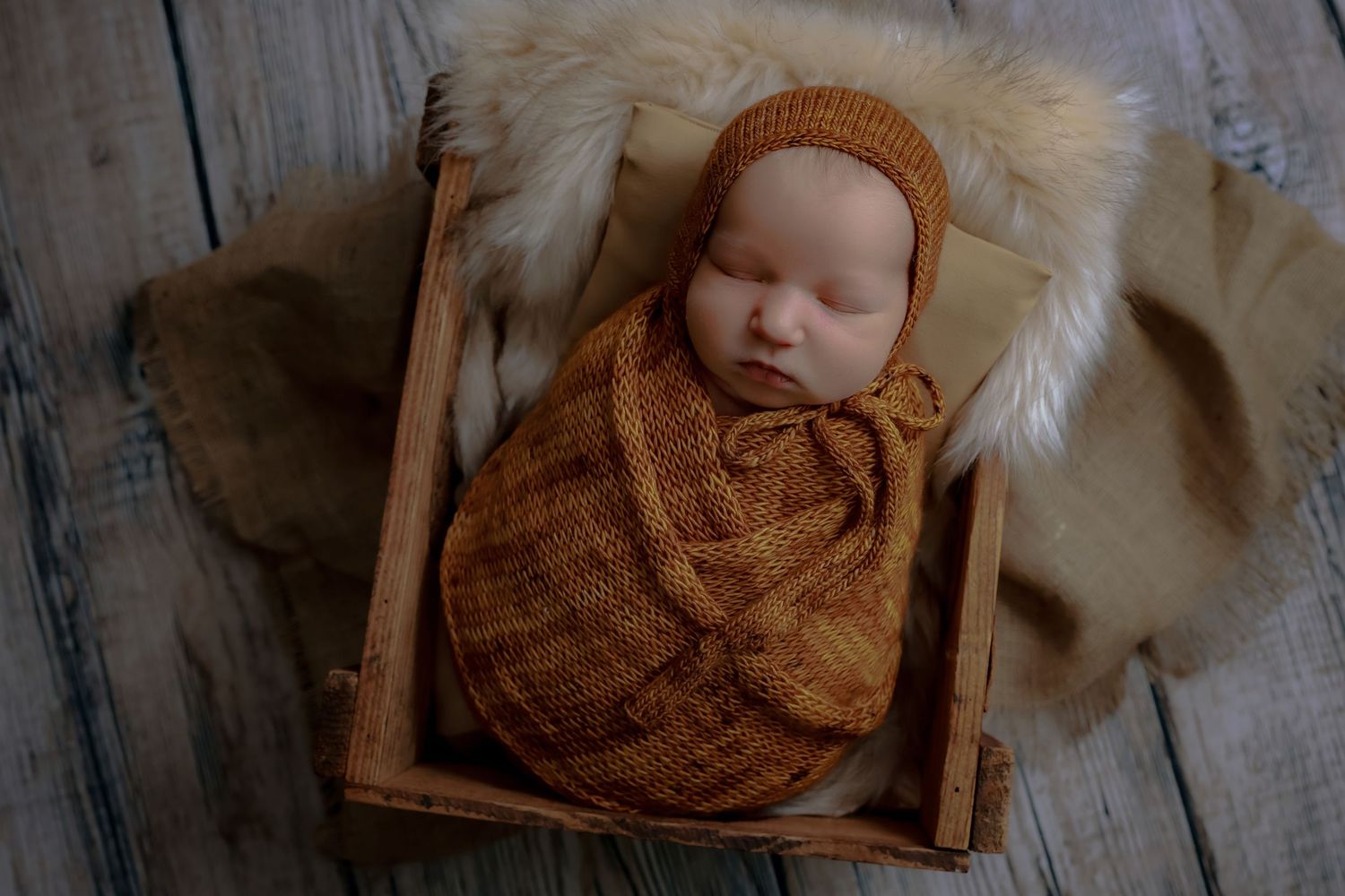 Sleeping baby in brown knit outfit lies on rustic wooden surface with white fur accents. luxury-family-photography-Rialto