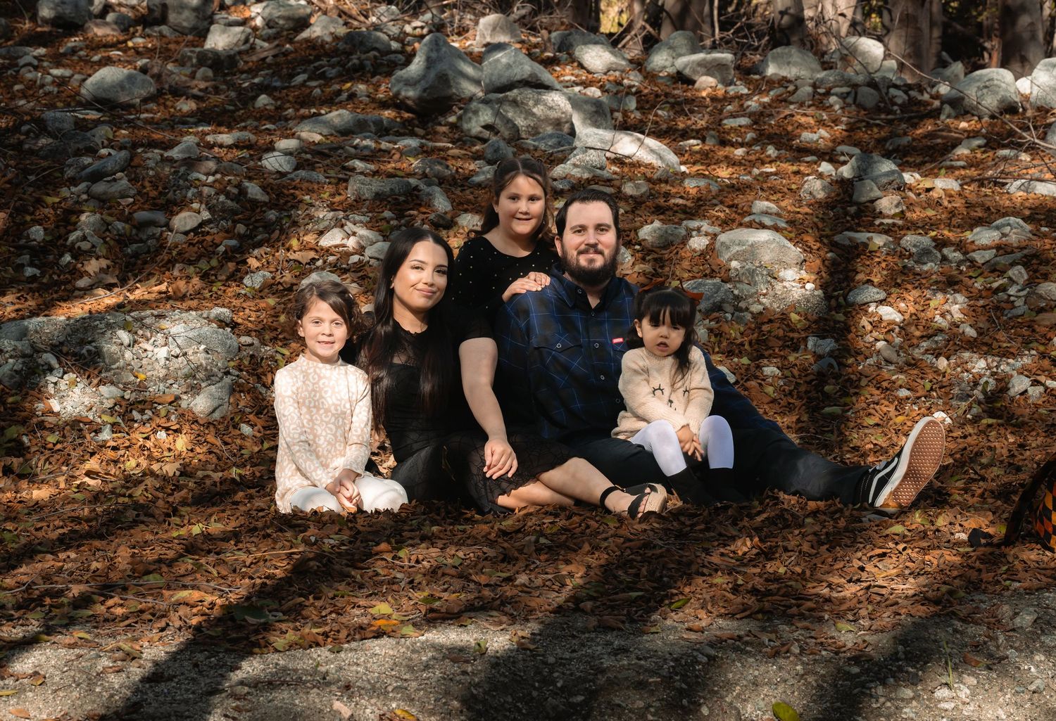 A group sits together on fallen autumn leaves against a rocky wall in warm, moody lighting.