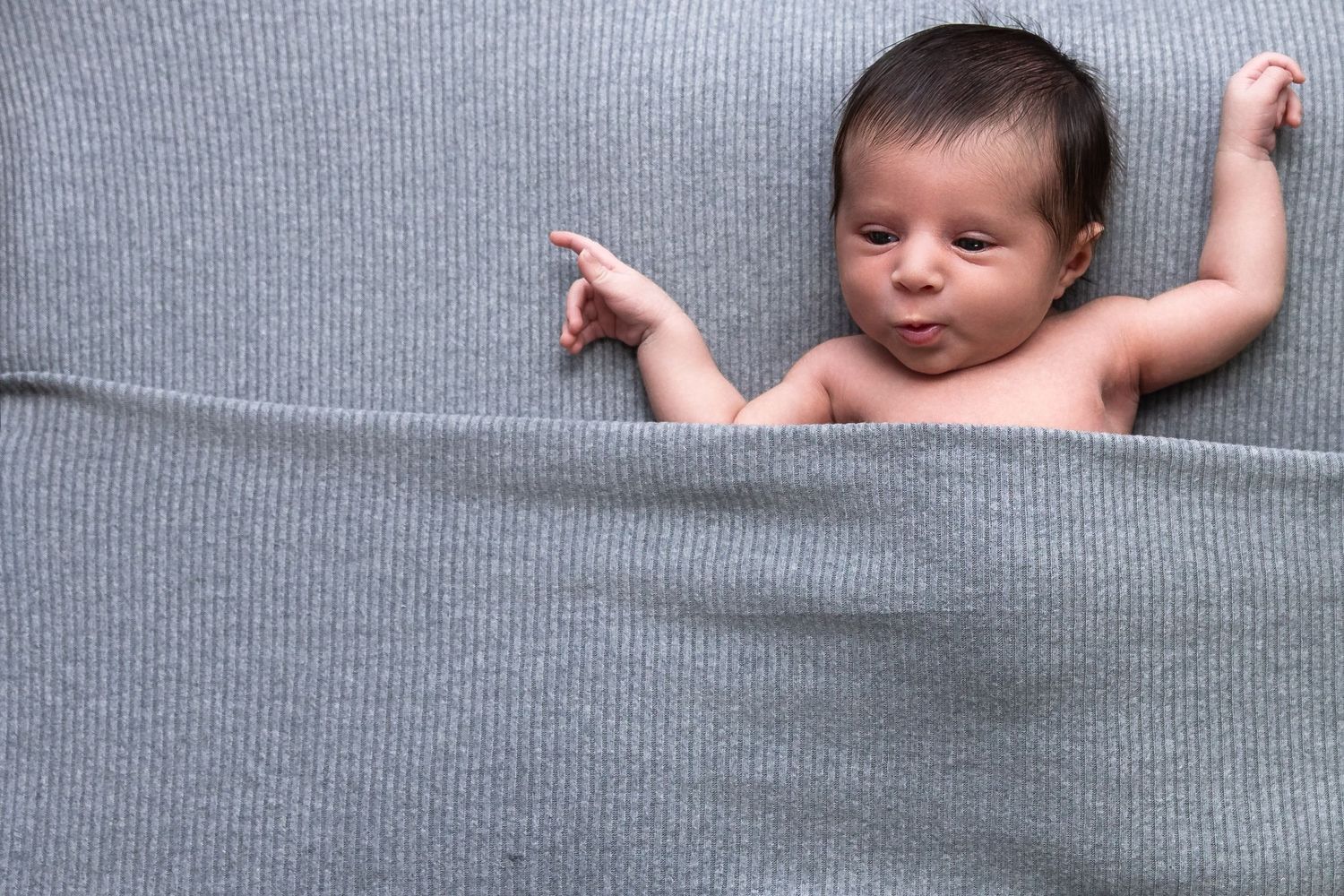A baby rests peacefully in a cozy grey blanket while sleeping on a soft surface. luxury-family-photography-Corona.