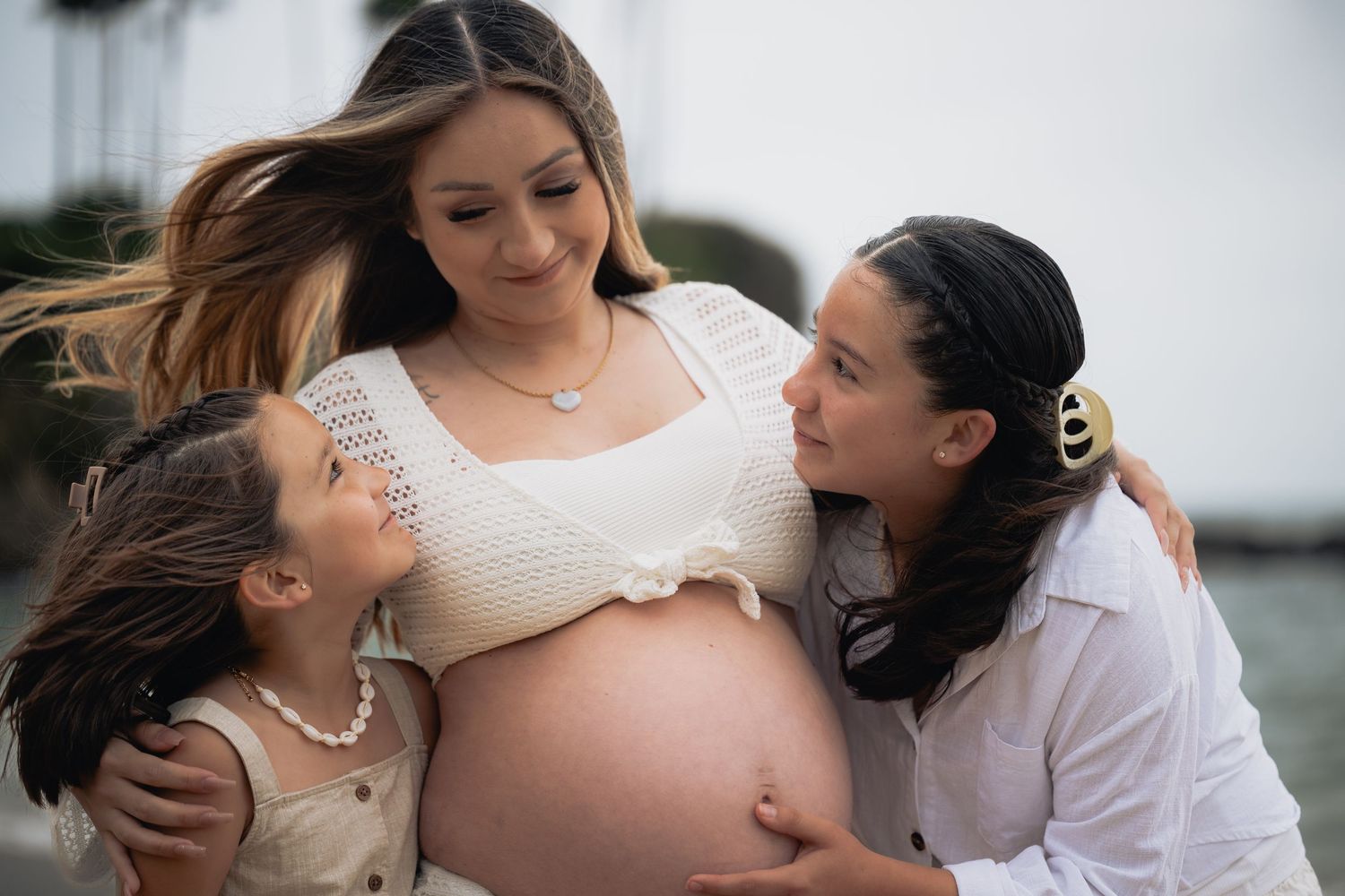 A tender moment between a pregnant woman and her daughters during a maternity photo shoot outdoors.