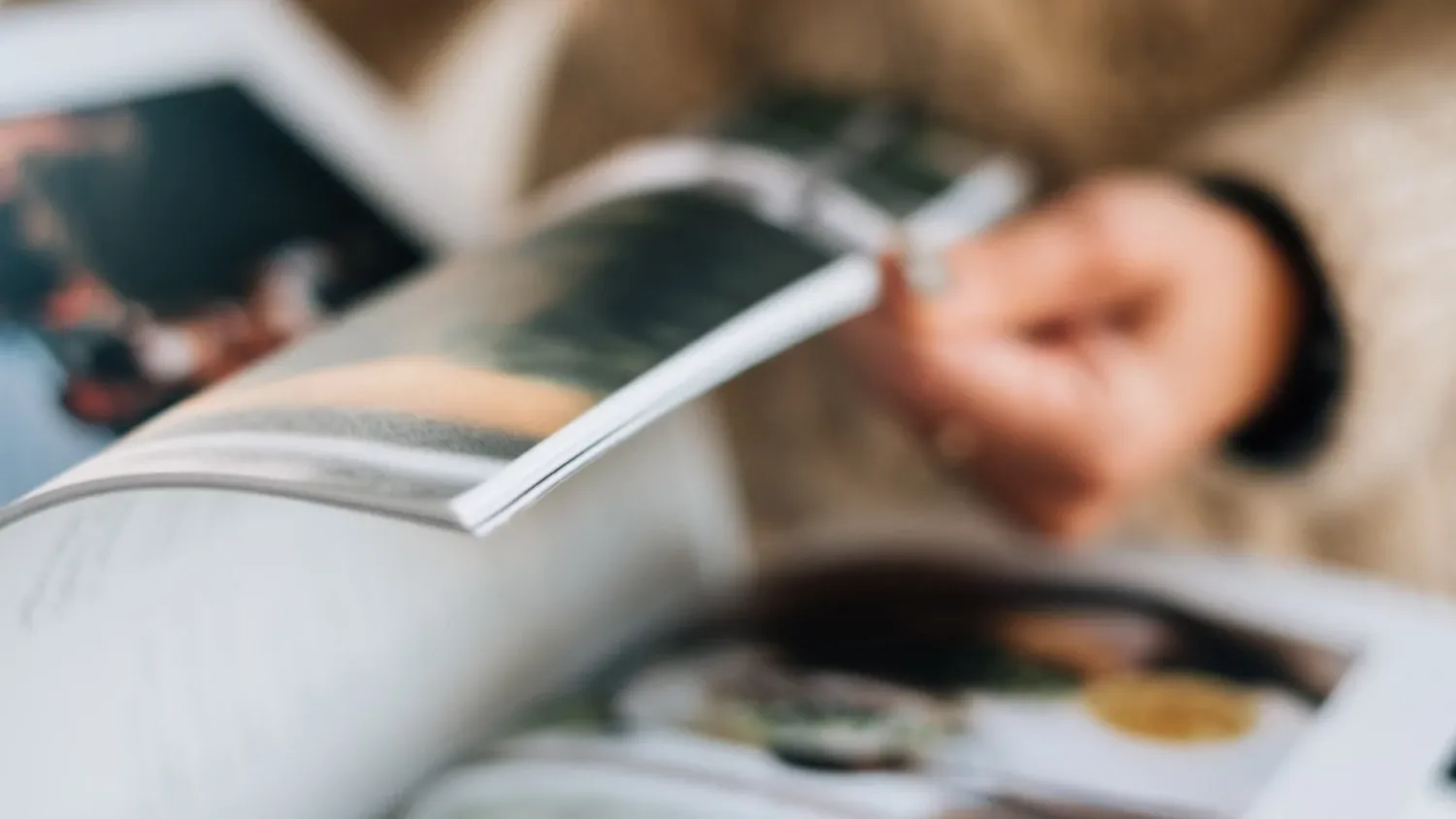 Person reading a book while holding a white coffee mug on a wooden table with natural lighting. luxury-family-photography-LosAngeles