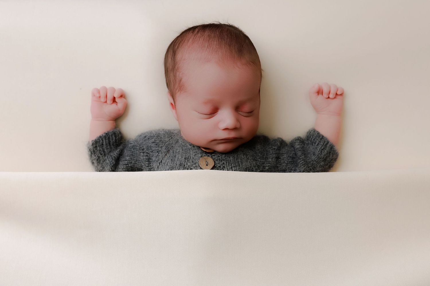 A peaceful sleeping newborn baby swaddled in white blankets rests in a soft bed. luxury-family-photography-Charter-Oak