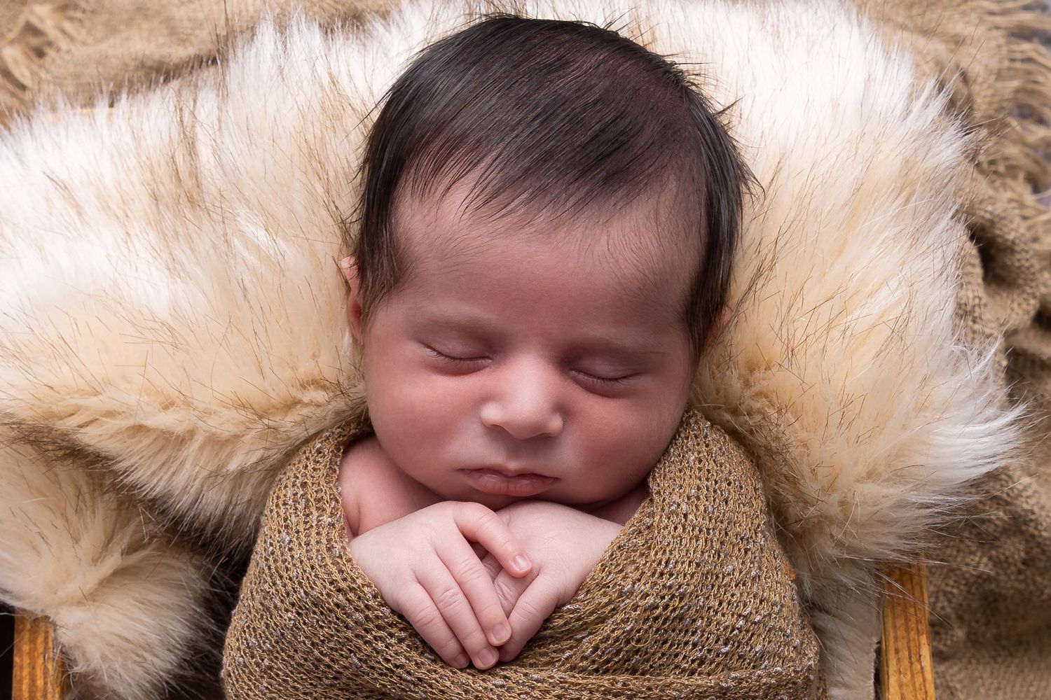 Sleeping newborn baby wrapped in brown knit blanket with soft fur background in studio setting.luxury-family-photography-Glendora