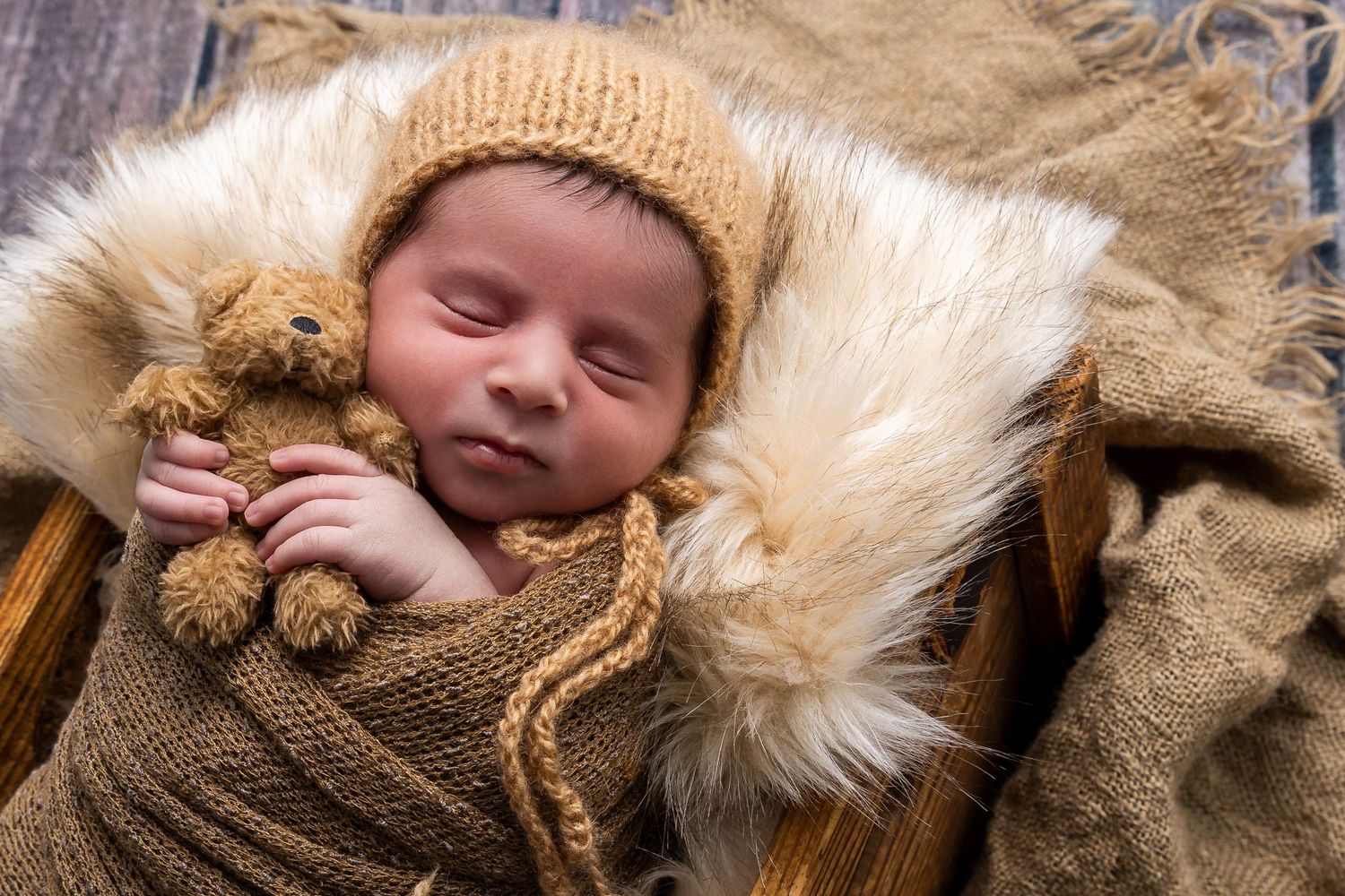 A sleeping newborn baby swaddled in soft brown and cream colored fur textiles against a neutral backdrop. luxury-family-photography-Covina