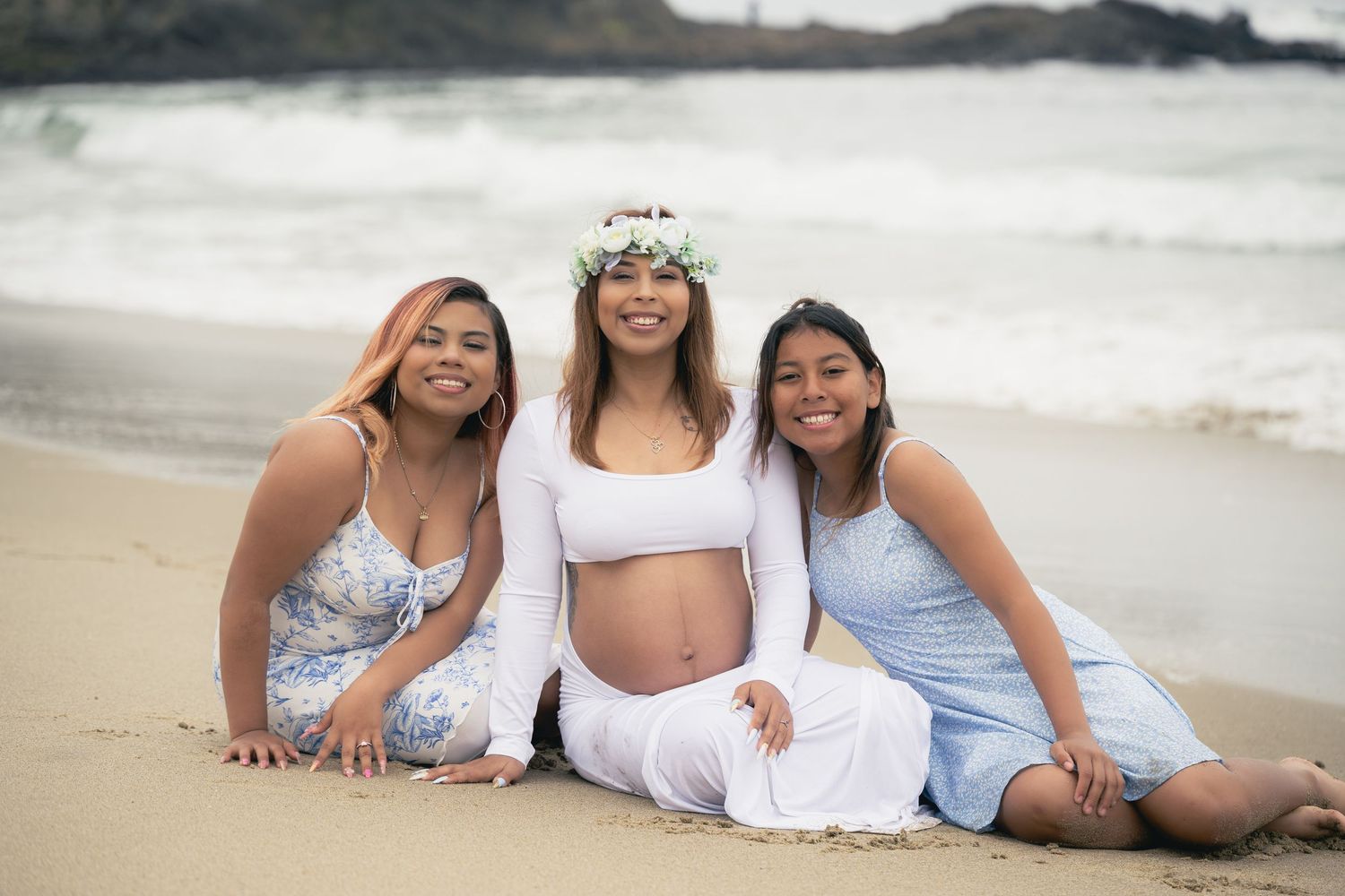A group of people in white and blue outfits lying together on a sandy beach during a photo session.