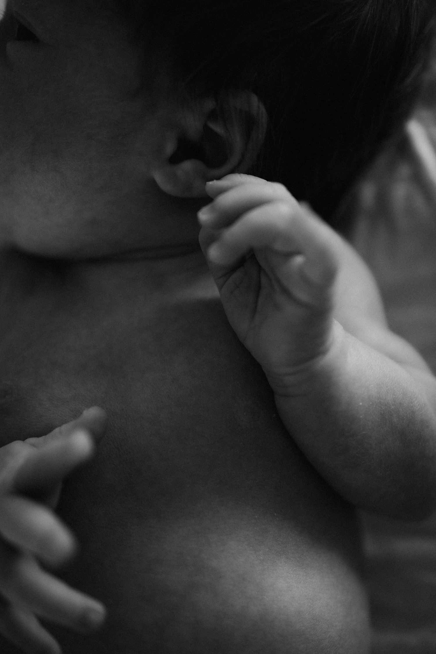 Black and white close-up photo of a newborn baby held against an adult, tiny hand raised near ear.