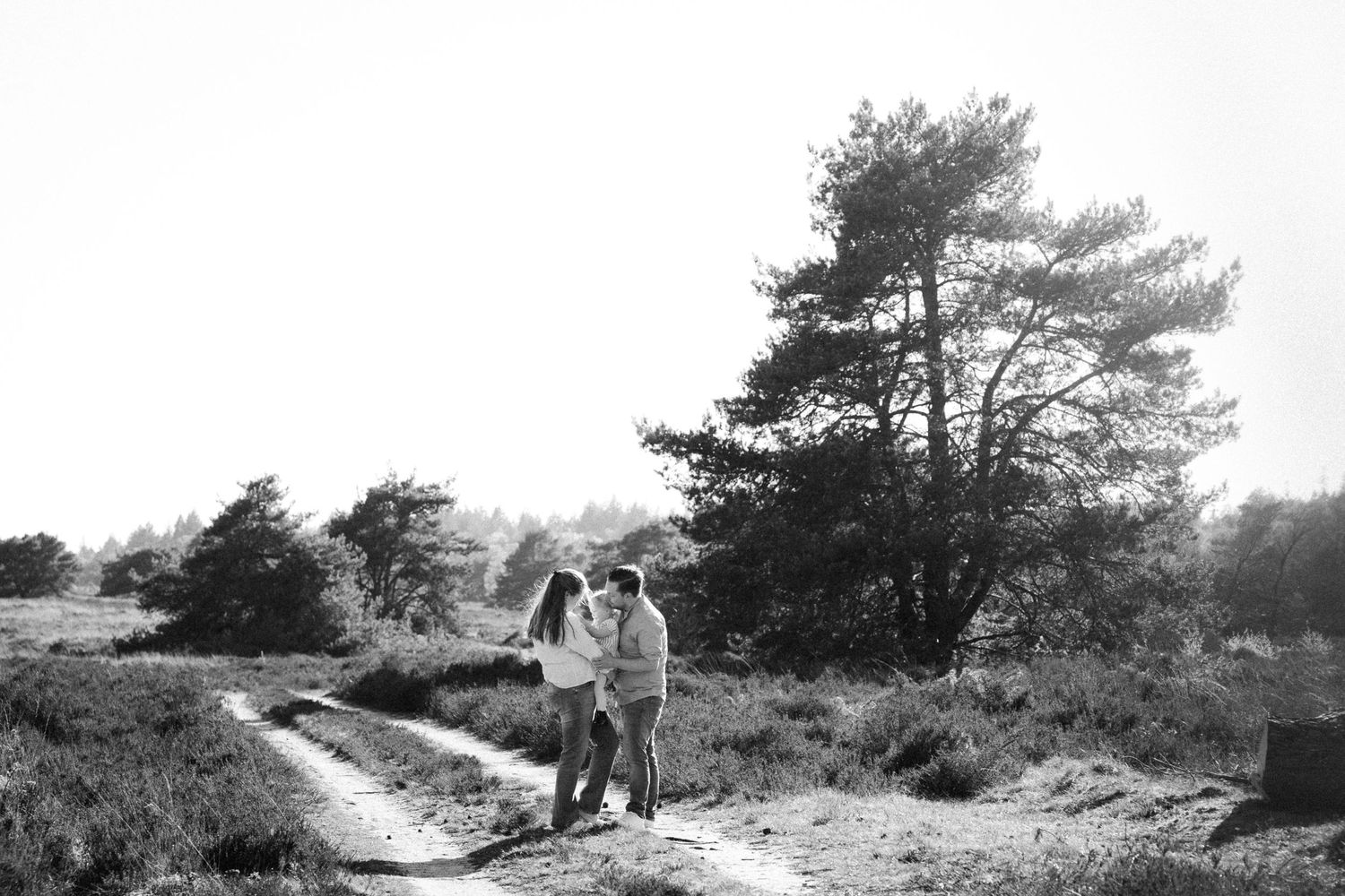 Black and white photo of a couple walking on a sandy path through a heathland landscape with trees.