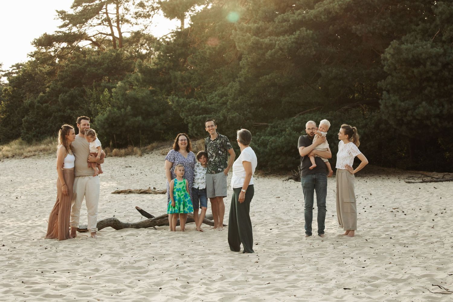 Group gathered on a sandy beach at sunset with trees in background.