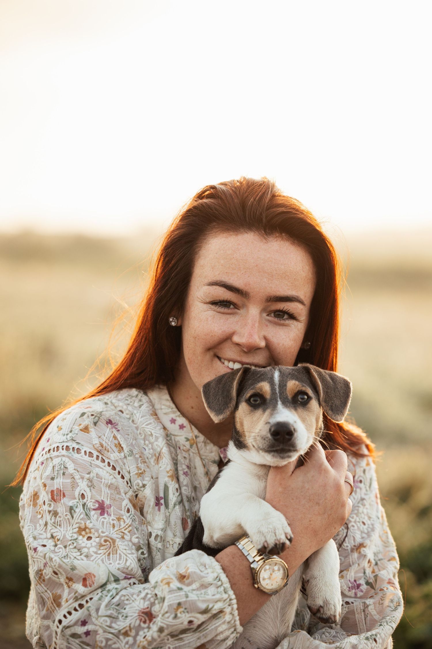 A person in a floral dress hugs and plays with their small black and white dog during a golden hour photoshoot.