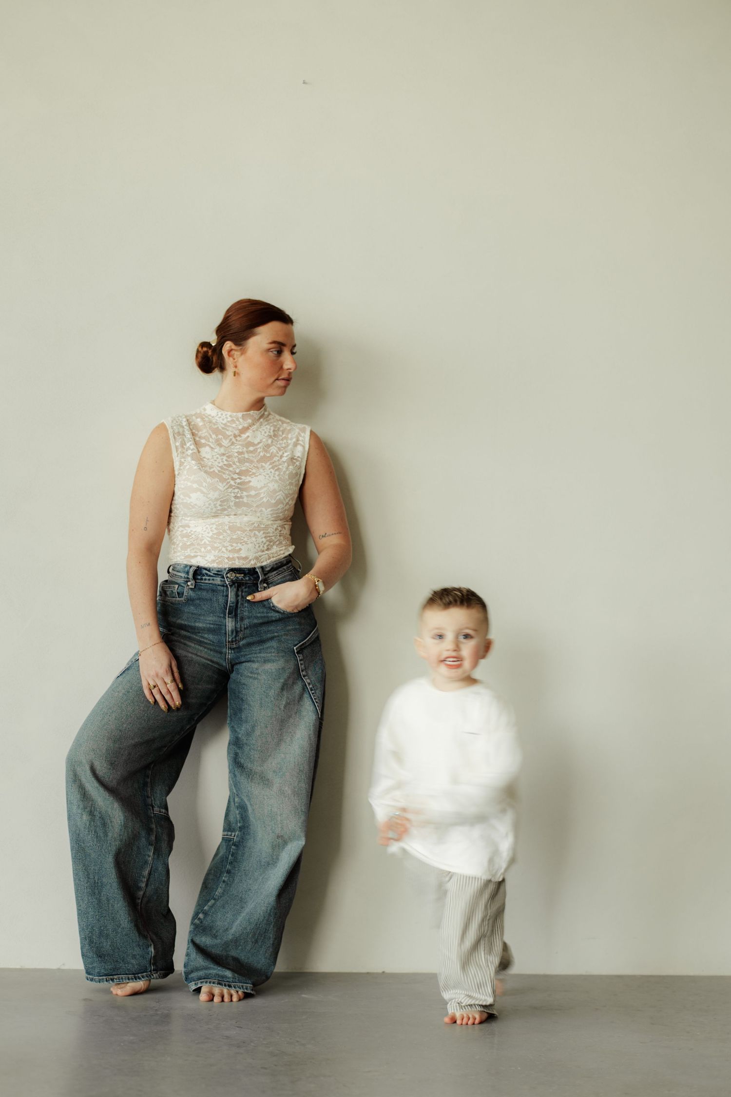 Studio portrait of adult and child standing against light wall wearing casual attire.