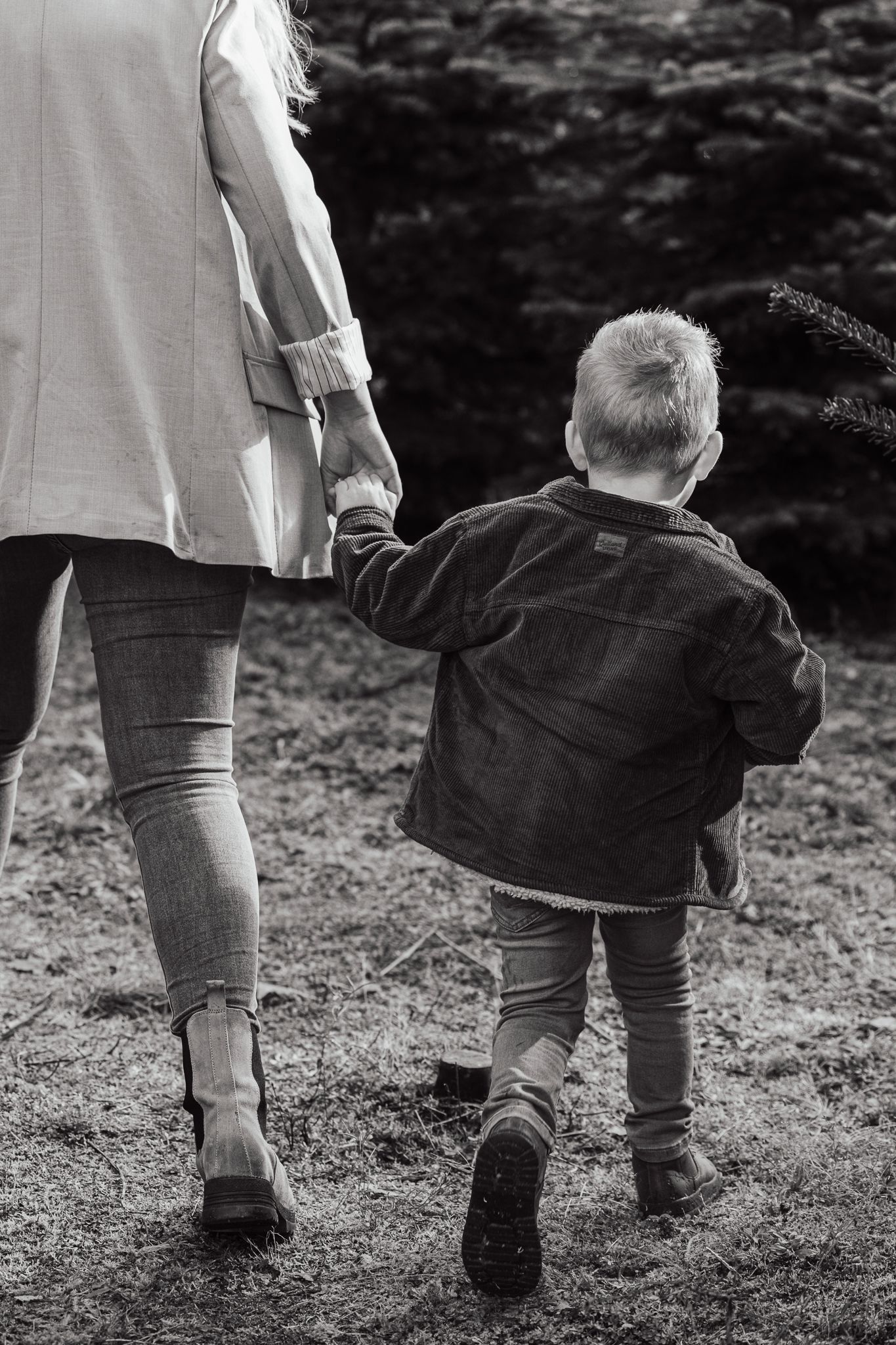 Black and white image of a child holding hands with parent while walking outdoors.