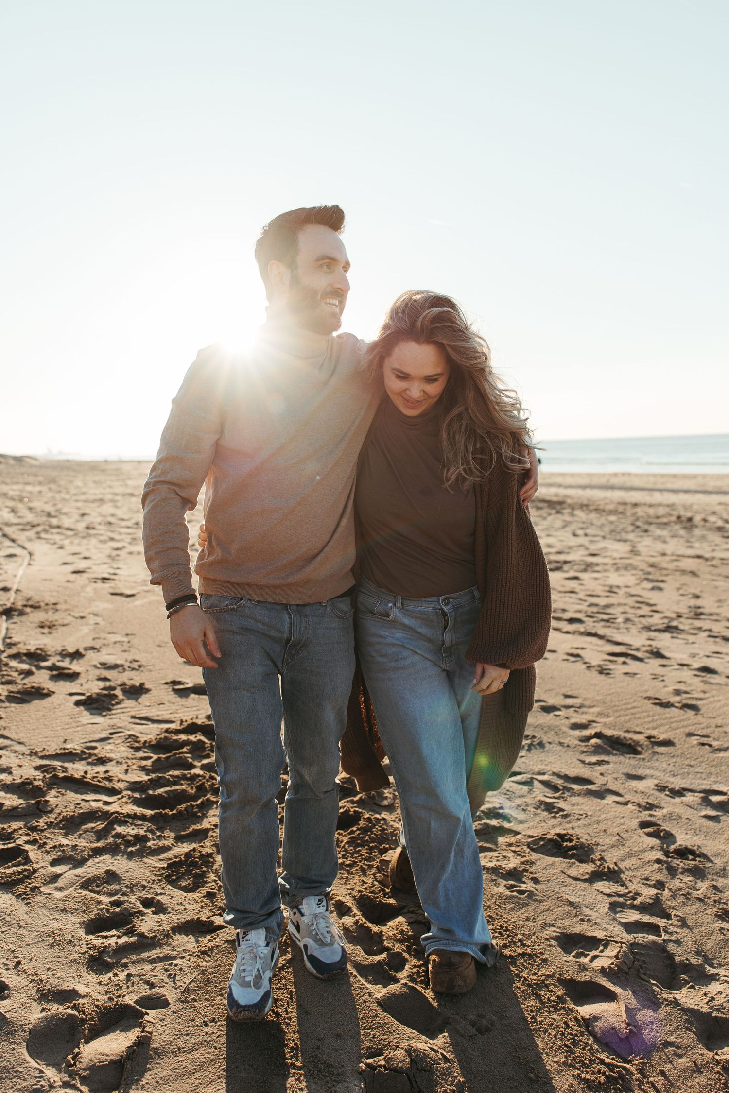 Couple laughing while walking together on a sandy beach at sunset.