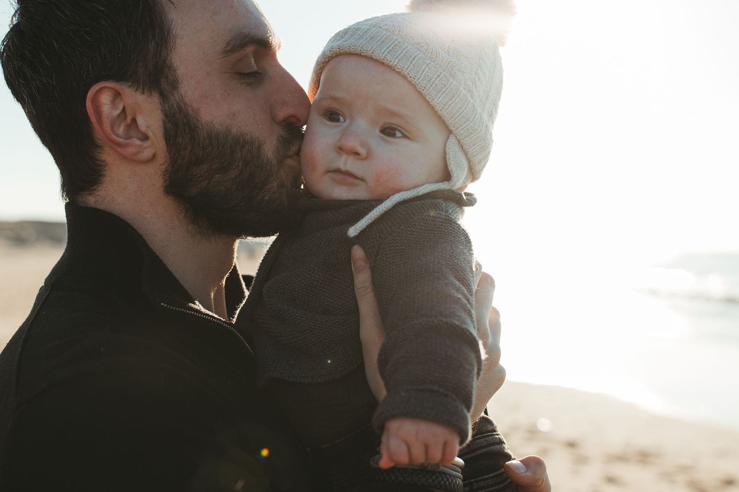 An intimate moment between parent and baby against a bright coastal backdrop.