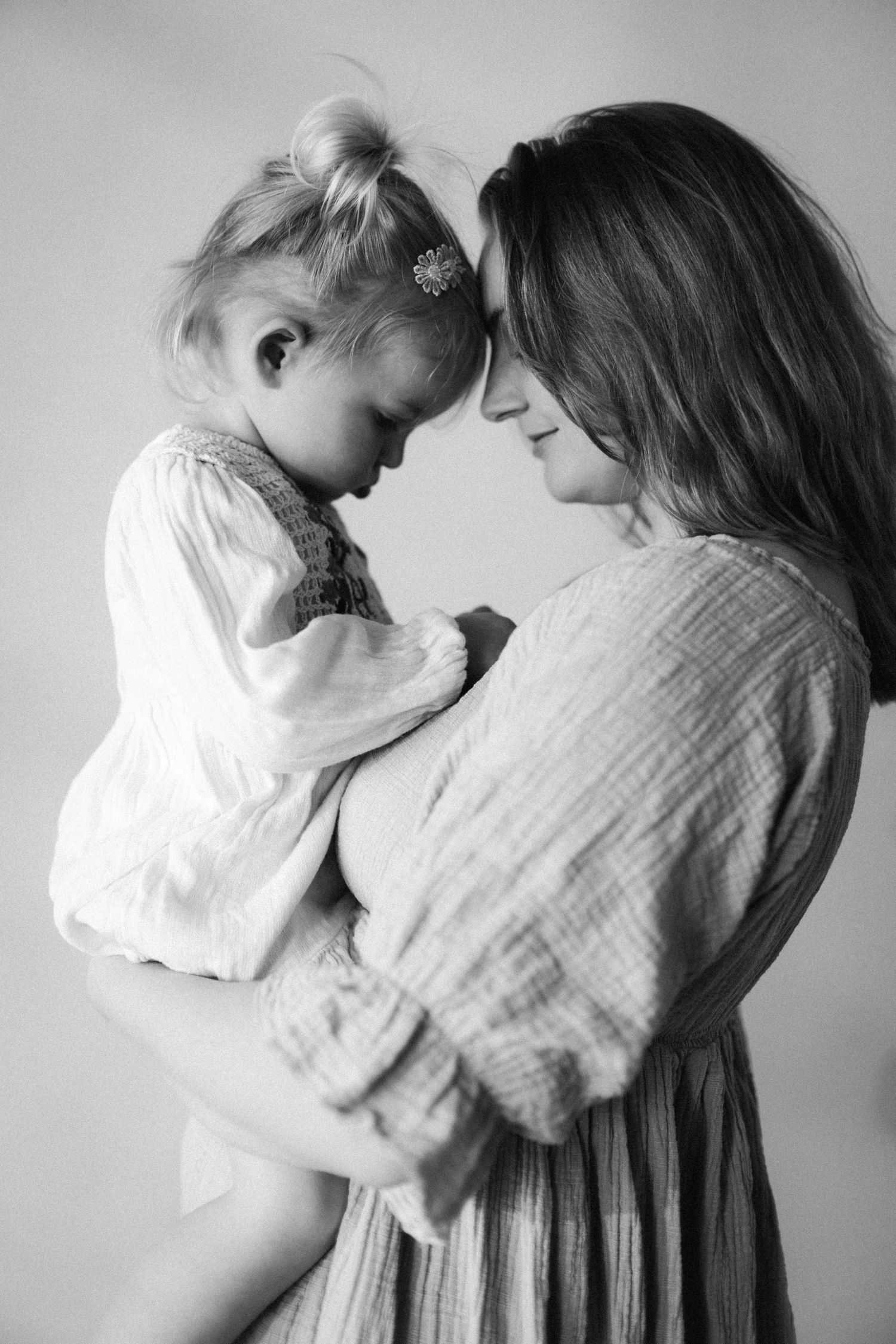 Black and white photo of a mother tenderly holding her toddler daughter, foreheads touching in an intimate moment.