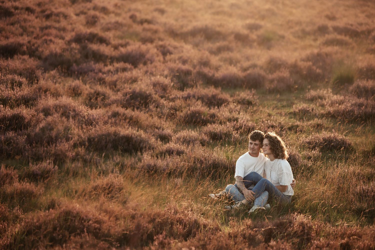Couple embracing in a rustic field during warm sunset light.
