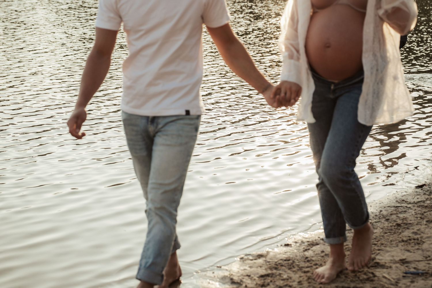 Couple walking along shoreline of lake at sunset holding hands.