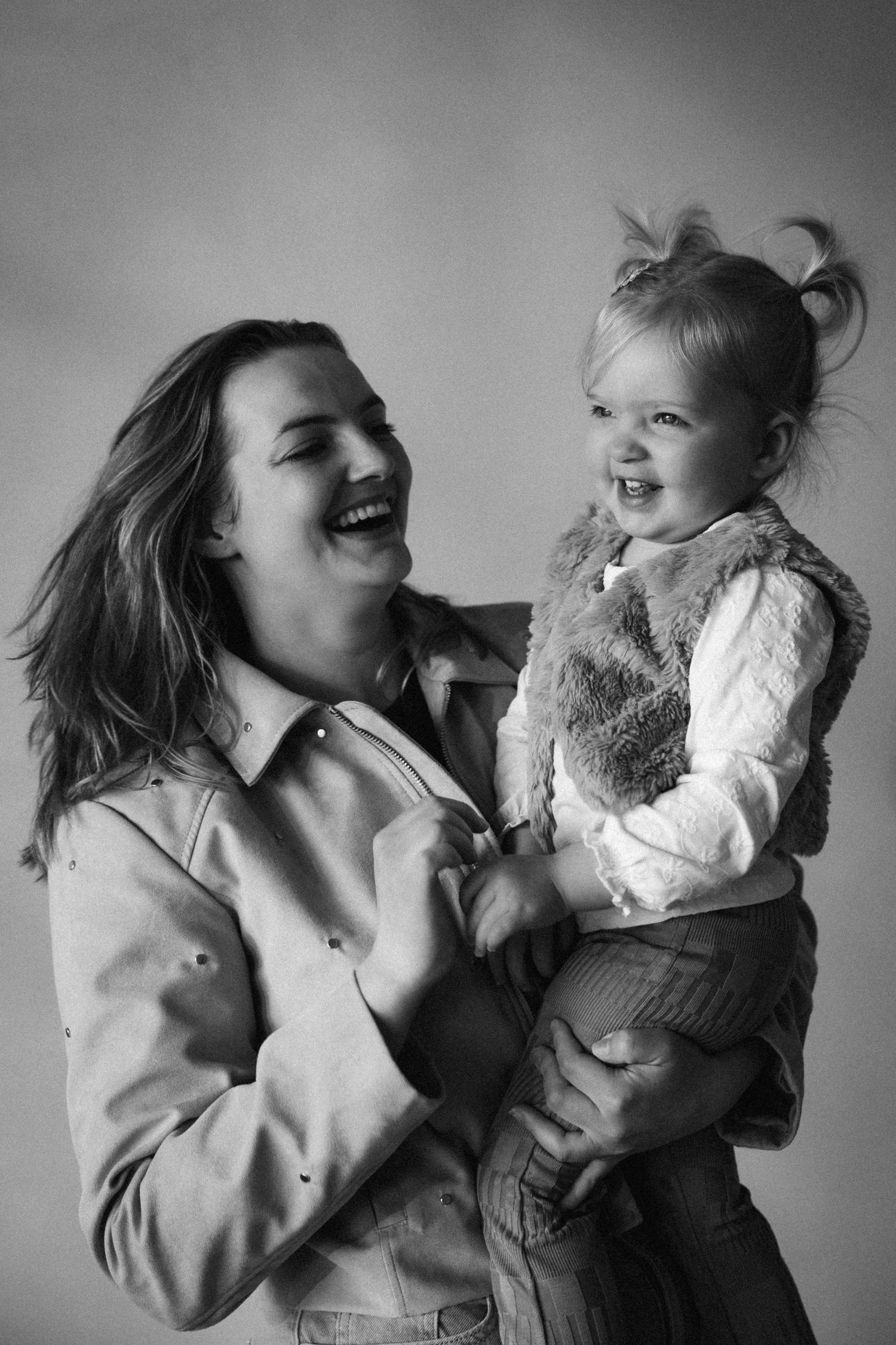 Black and white photo of a laughing mother holding her happy toddler daughter in a studio portrait.