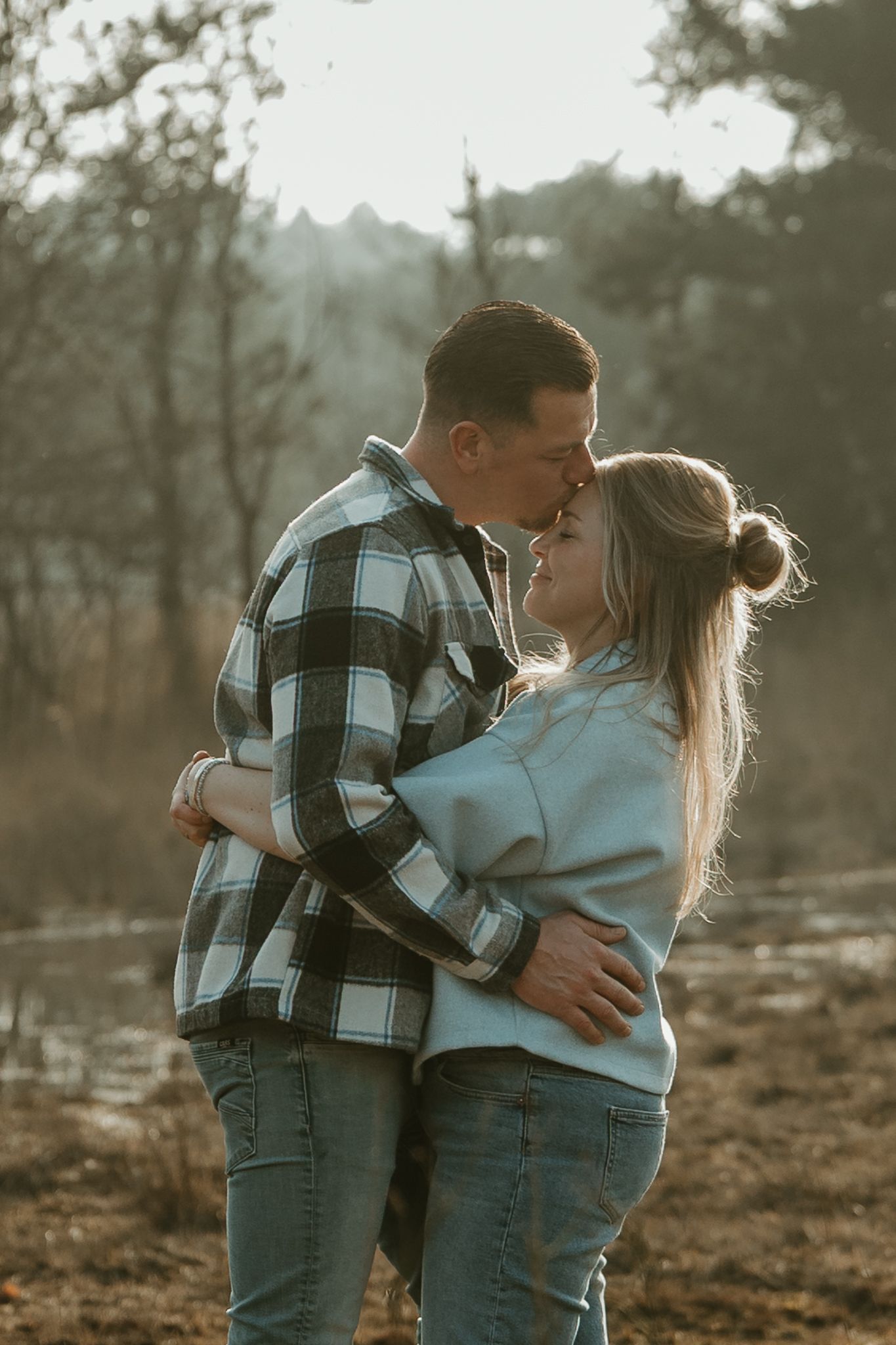 Couple sharing an intimate moment in casual attire against a natural backdrop.