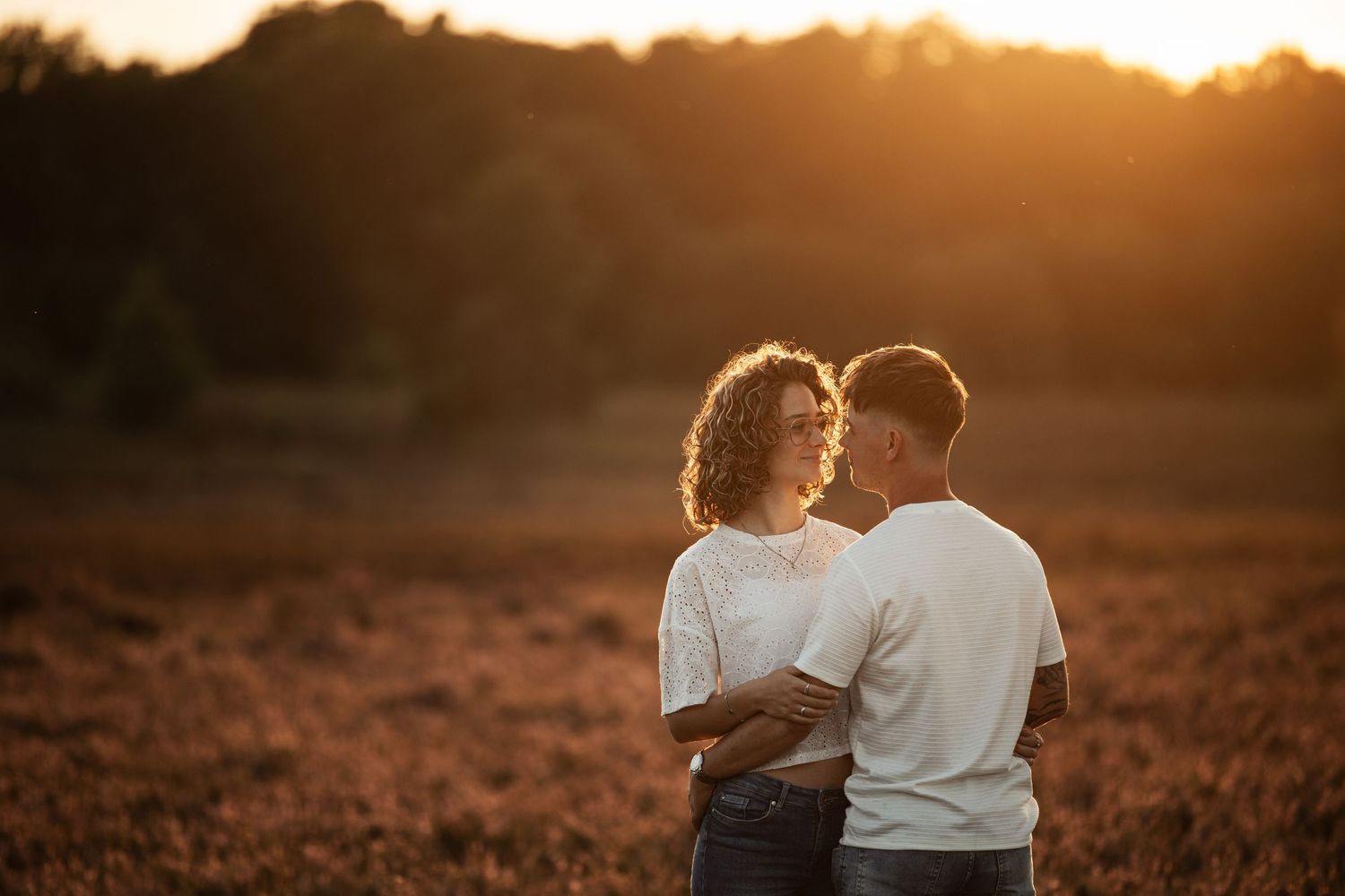 Romantic sunset photoshoot with couple sitting in golden-lit meadow.
