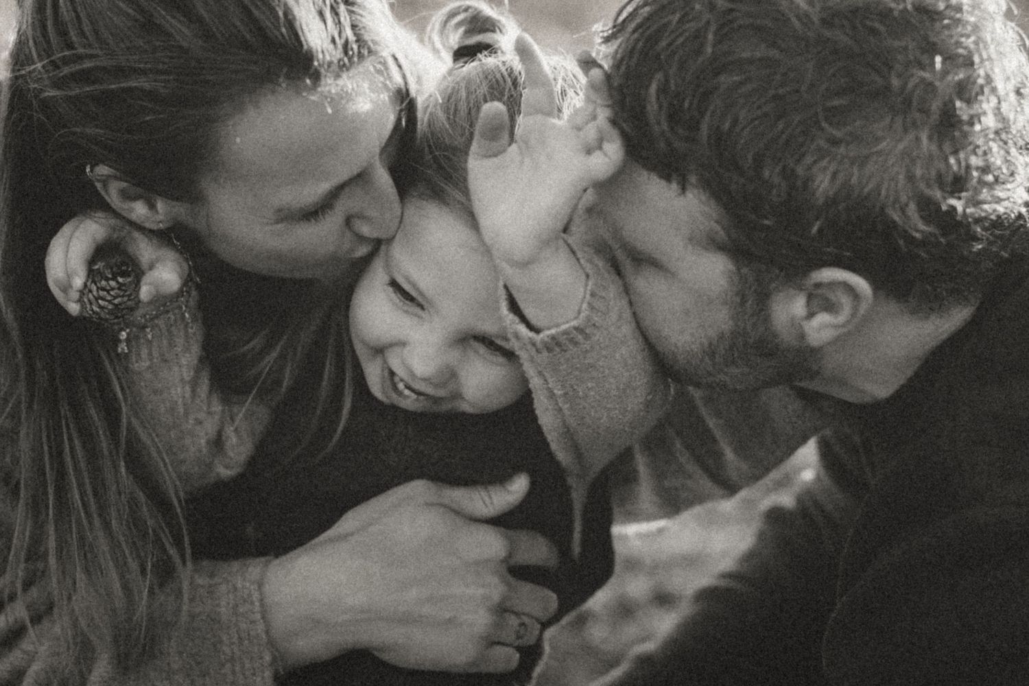 A tender black and white family moment captured as parents share affectionate kisses with their joyful child.
