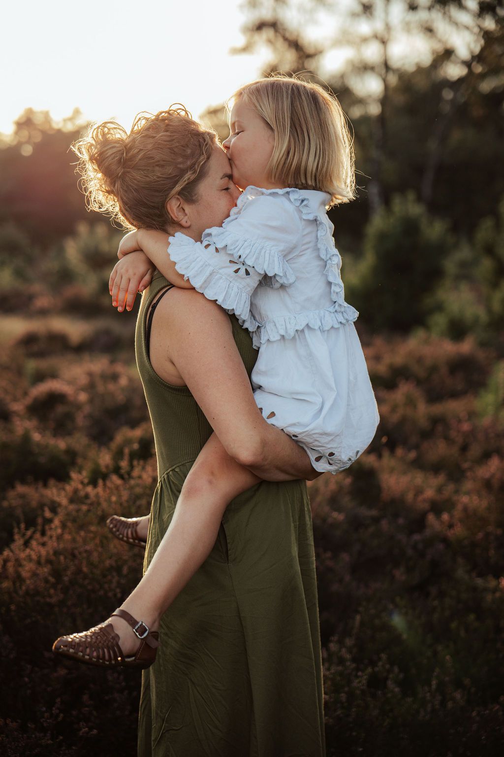 A tender moment captured at sunset in a field of heather, with an olive green dress and white ruffled outfit.