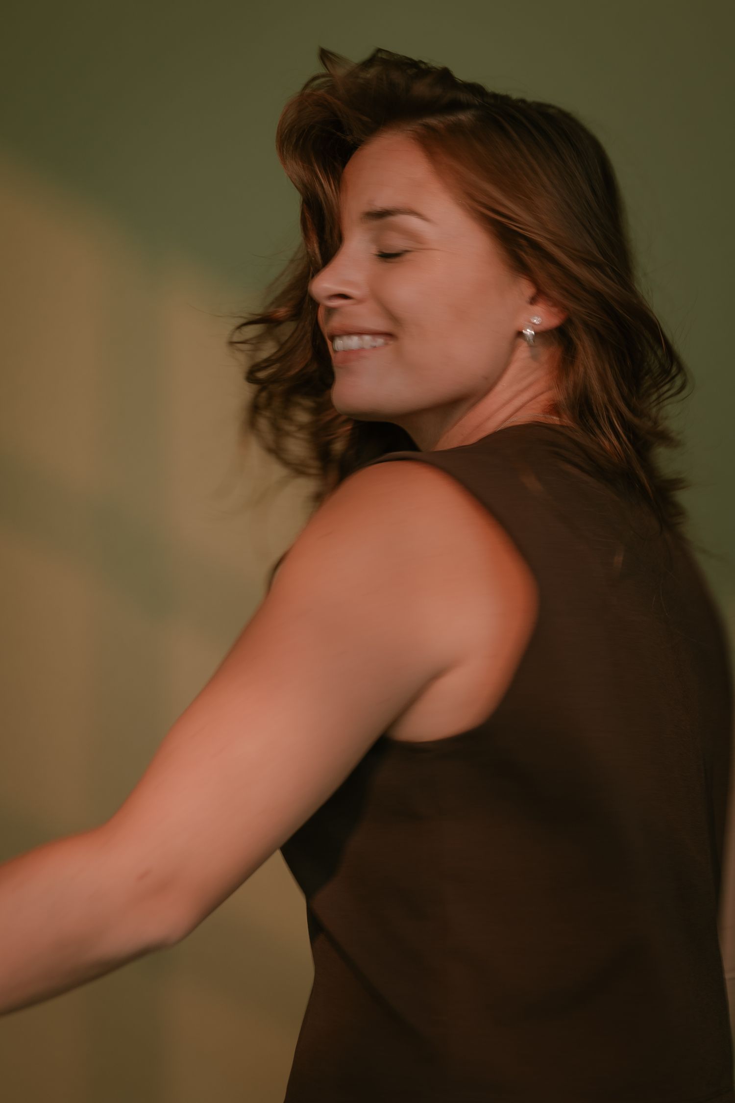 Smiling woman with brown hair wearing a dark sleeveless top, posing gracefully against a green background.
