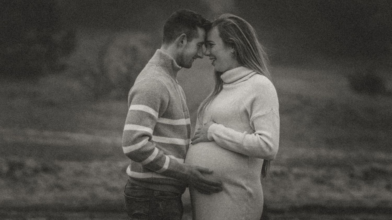 A moody black and white panoramic shot of a couple in an outdoor setting.