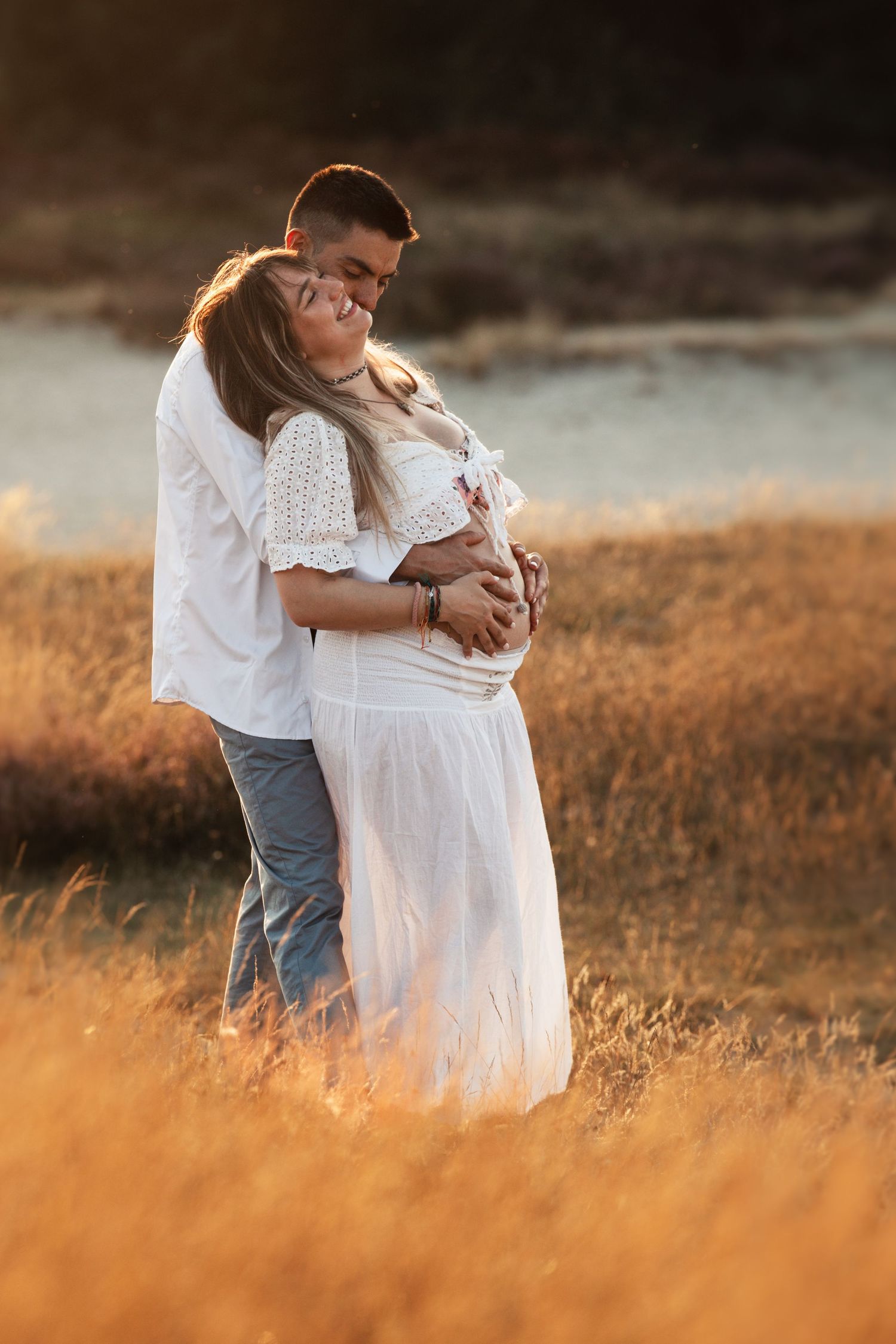 A romantic maternity photoshoot in a sun-lit field with golden grass.